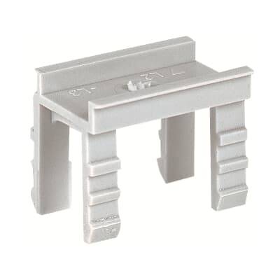 Ein graues Plastikteil mit vier Beinen, vermutlich ein Halter oder Abstandshalter, vor einem weißen Hintergrund.