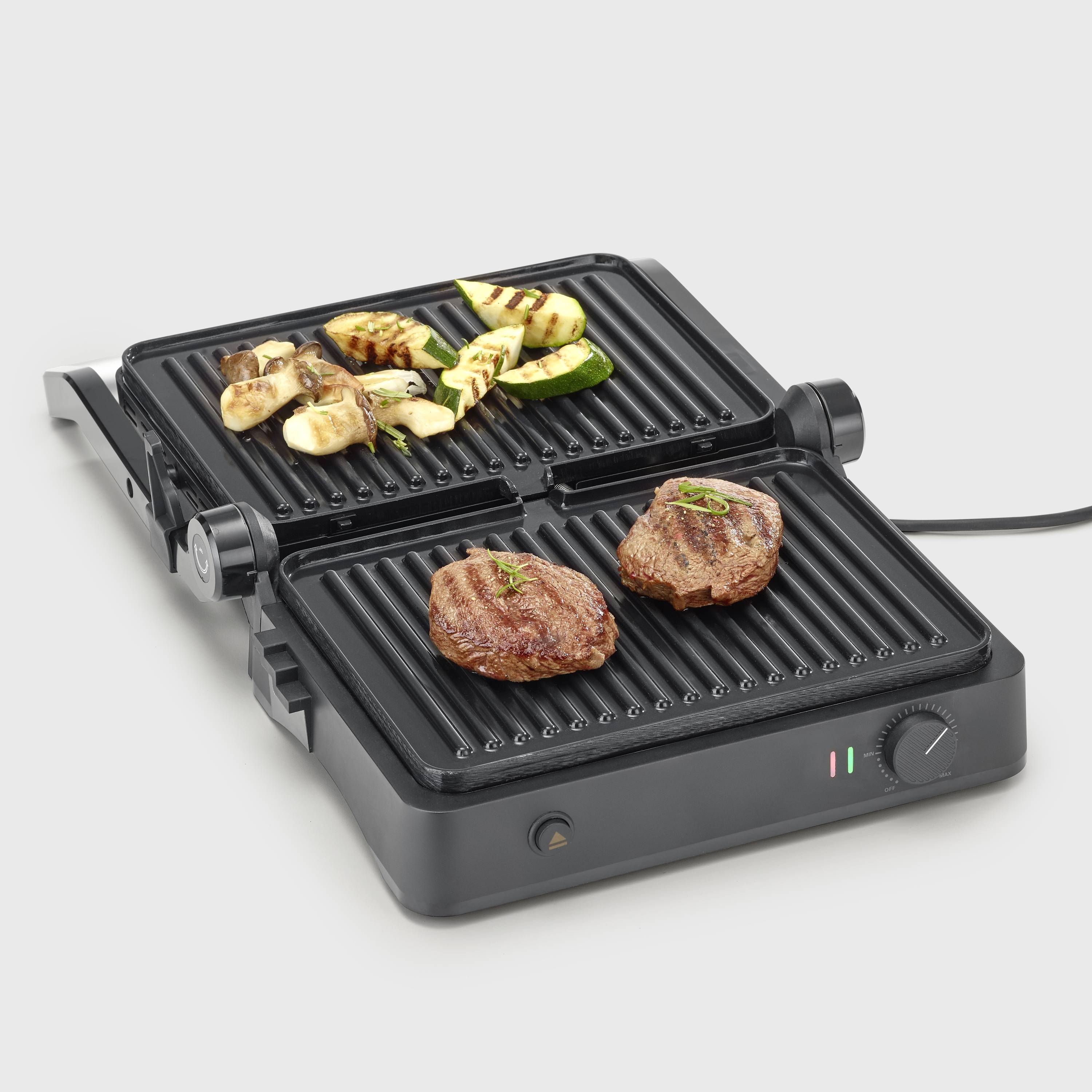 Elektrogrill mit offenem Grilldeckel, zwei Steaks, und Gemüse wie Zucchini und Pilzen darauf, zeigt Grillfunktion und Nutzung.