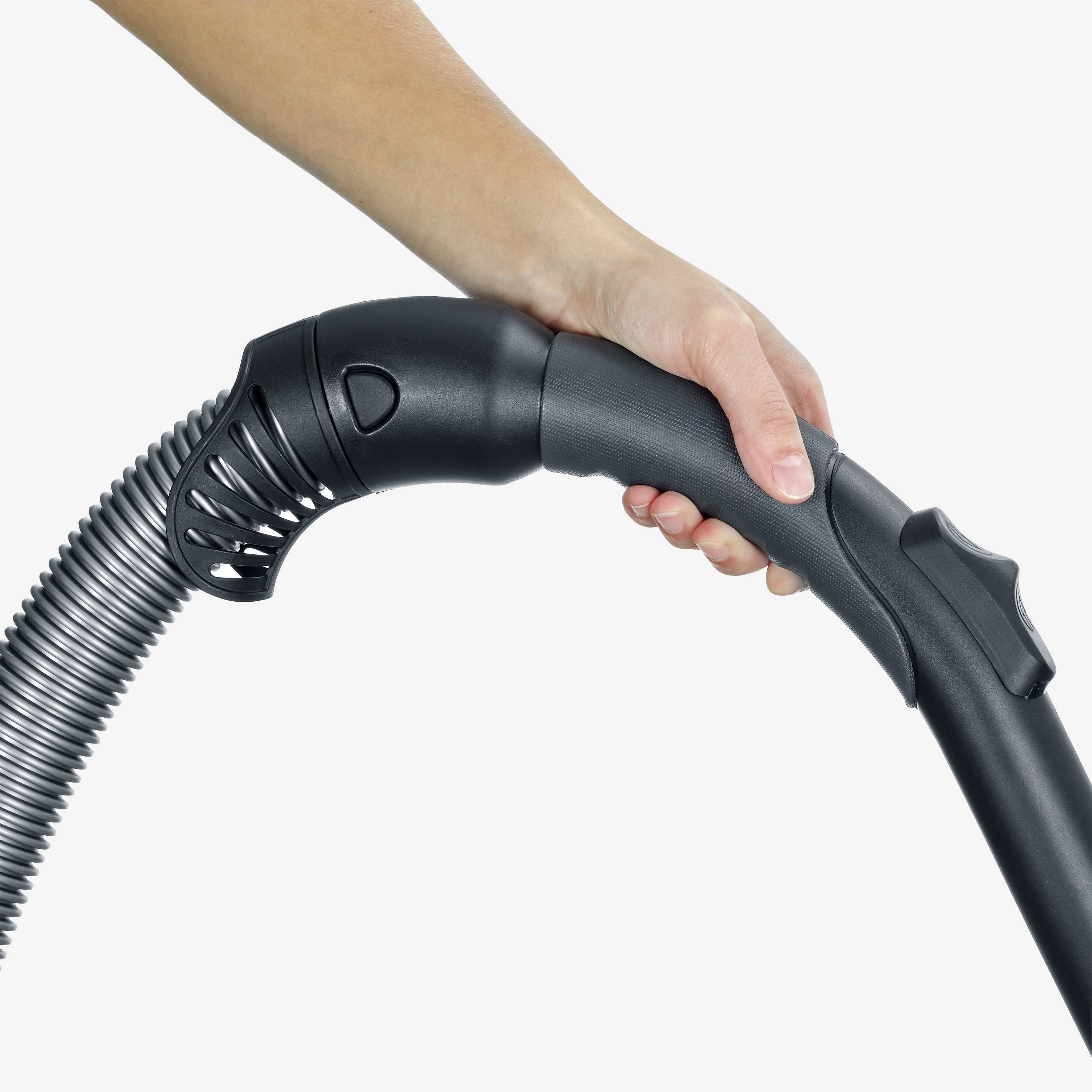 Eine Hand hält den Griff eines Staubsaugerrohrs mit einem gerippten Flexschlauch, der an das Rohr angeschlossen ist.