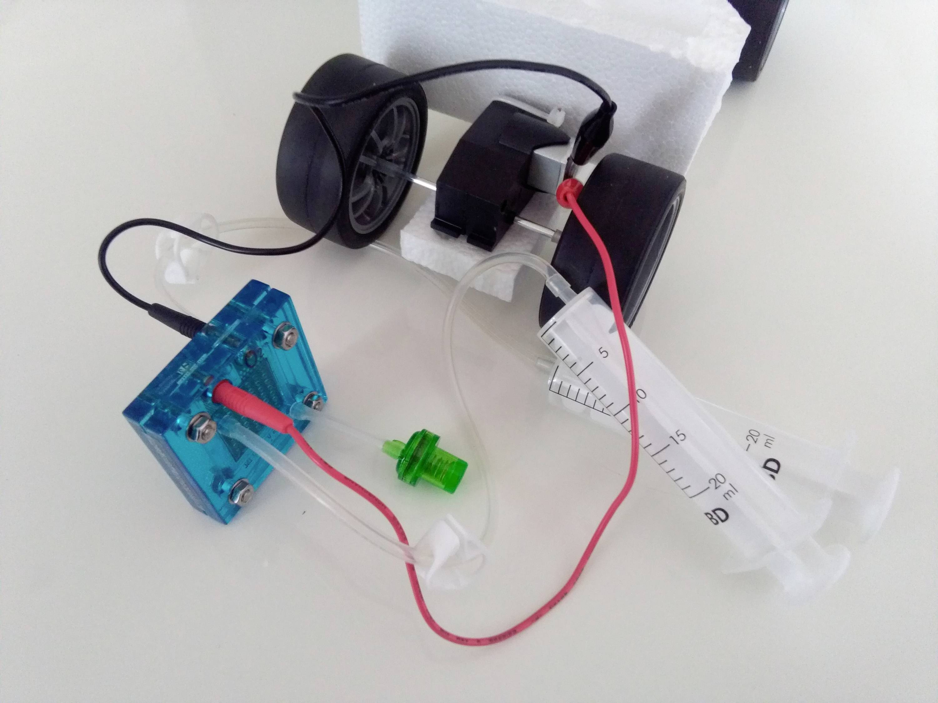 Ein kleines Fahrzeug mit zwei Rädern, verbunden mit einer Spritze und einem elektrischen Modul, zeigt ein einfaches Hydrauliksystem.