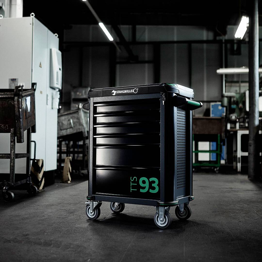 Werkstattwagen mit der Aufschrift 'TTS 93' steht in einer industriellen Umgebung. Der Wagen hat Schubladen und steht auf Rollen.