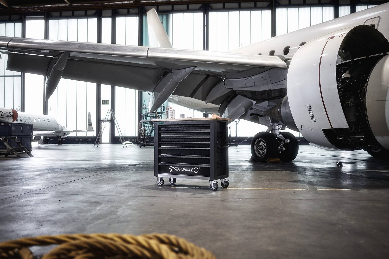 Ein Flugzeug steht in einem Hangar zur Wartung. Im Vordergrund befindet sich ein rollbarer Werkzeugwagen.