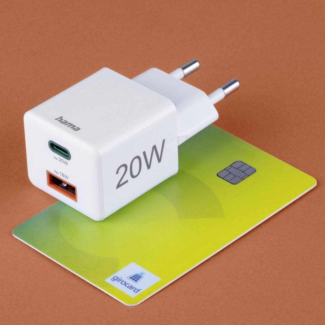 Ladegerät mit 20W-Anzeige und USB-Anschlüssen, auf einer grünen girocard platziert, vor braunem Hintergrund.