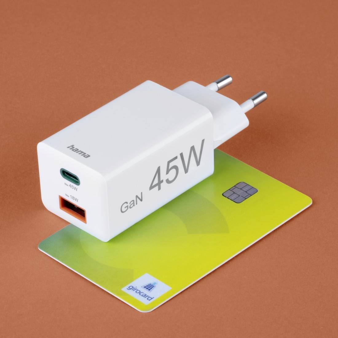 Ein weißes 45-Watt-GaN-Ladegerät liegt auf einer grünen Karte mit Chip, auf braunem Hintergrund.