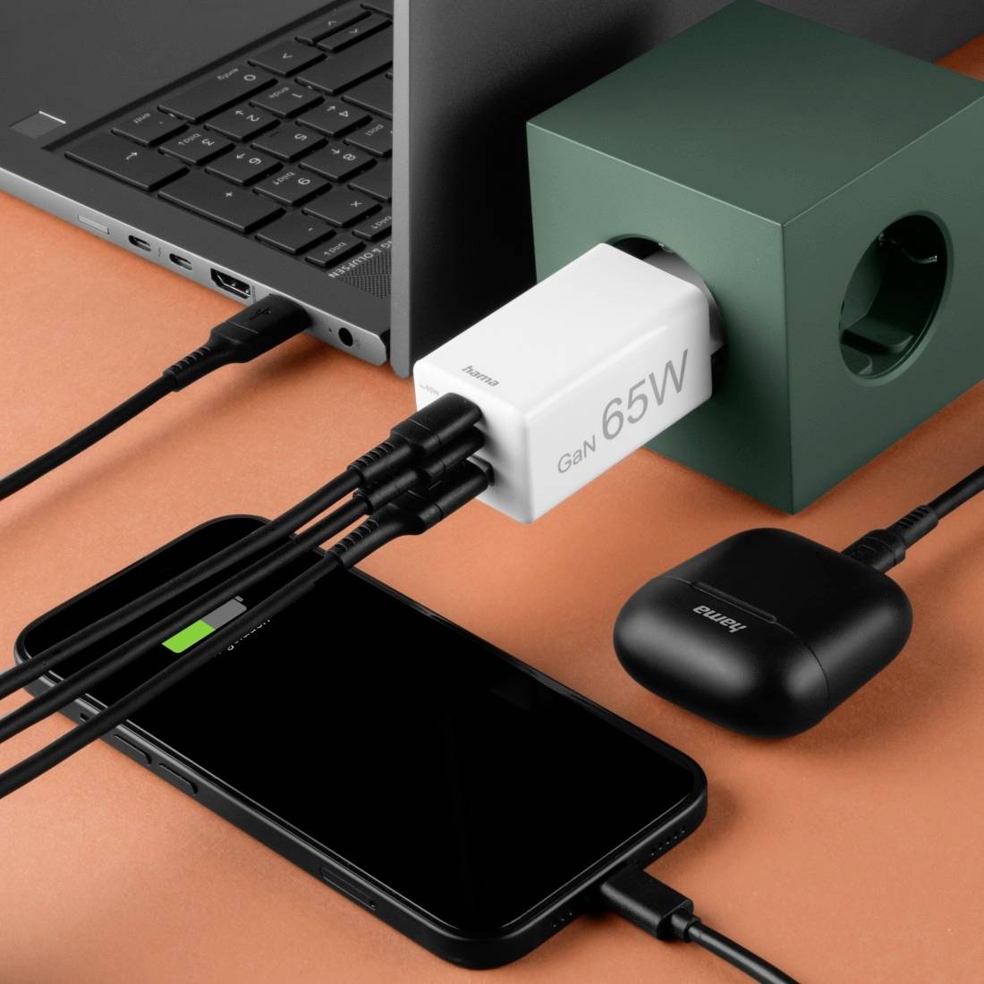 Smartphone und kabellose Kopfhörer werden mit einem Gan 65W-Ladegerät über mehrere Kabel aufgeladen, angeschlossen an eine Steckdose.
