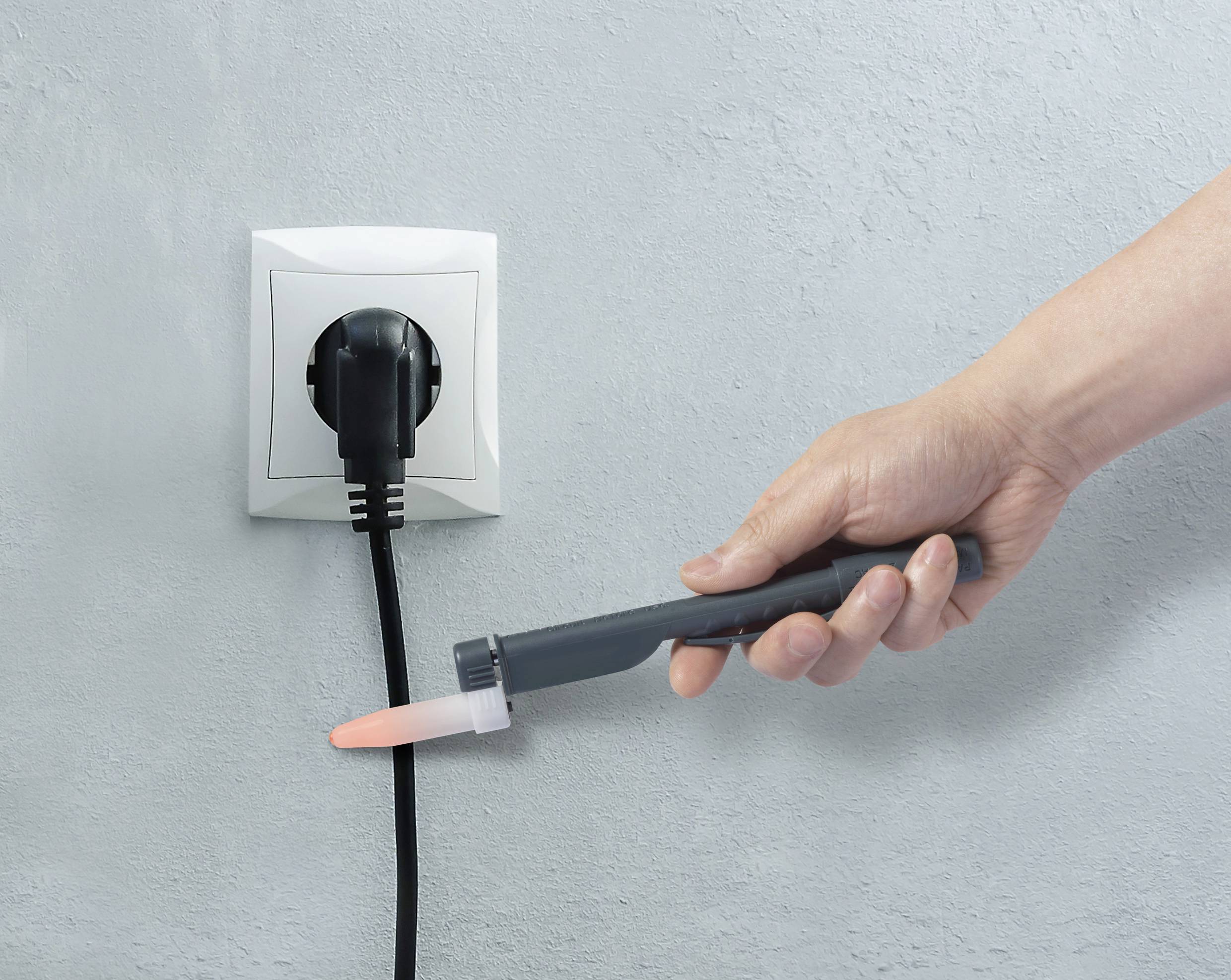 Eine Hand testet mit einem Prüfgerät die Spannung an einer Steckdose, in die ein schwarzer Stecker eingesteckt ist.