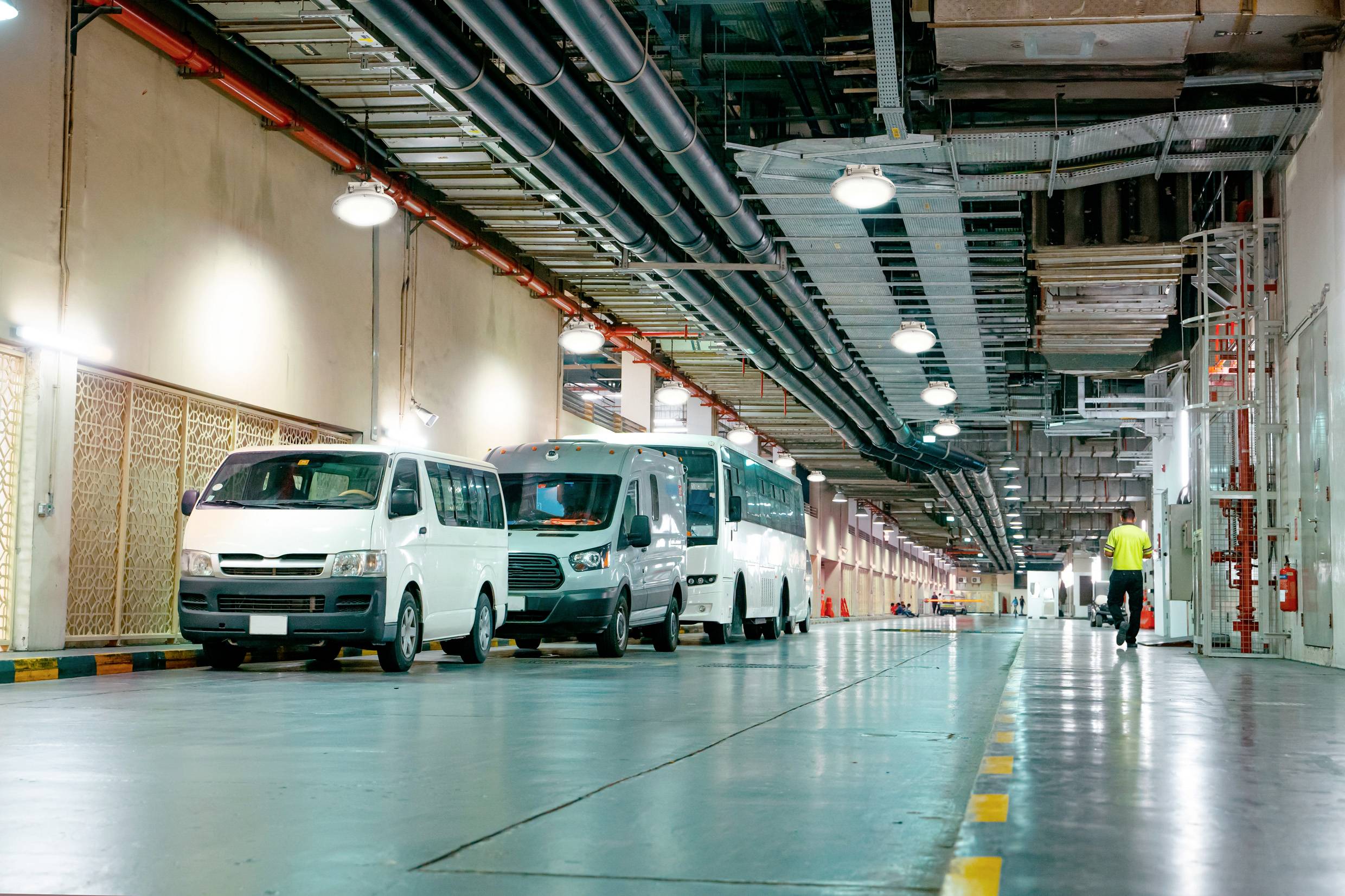 Mehrere weiße Lieferwagen parken in einer langen Reihe in einer unterirdischen Garage. Eine Person geht in der Ferne.