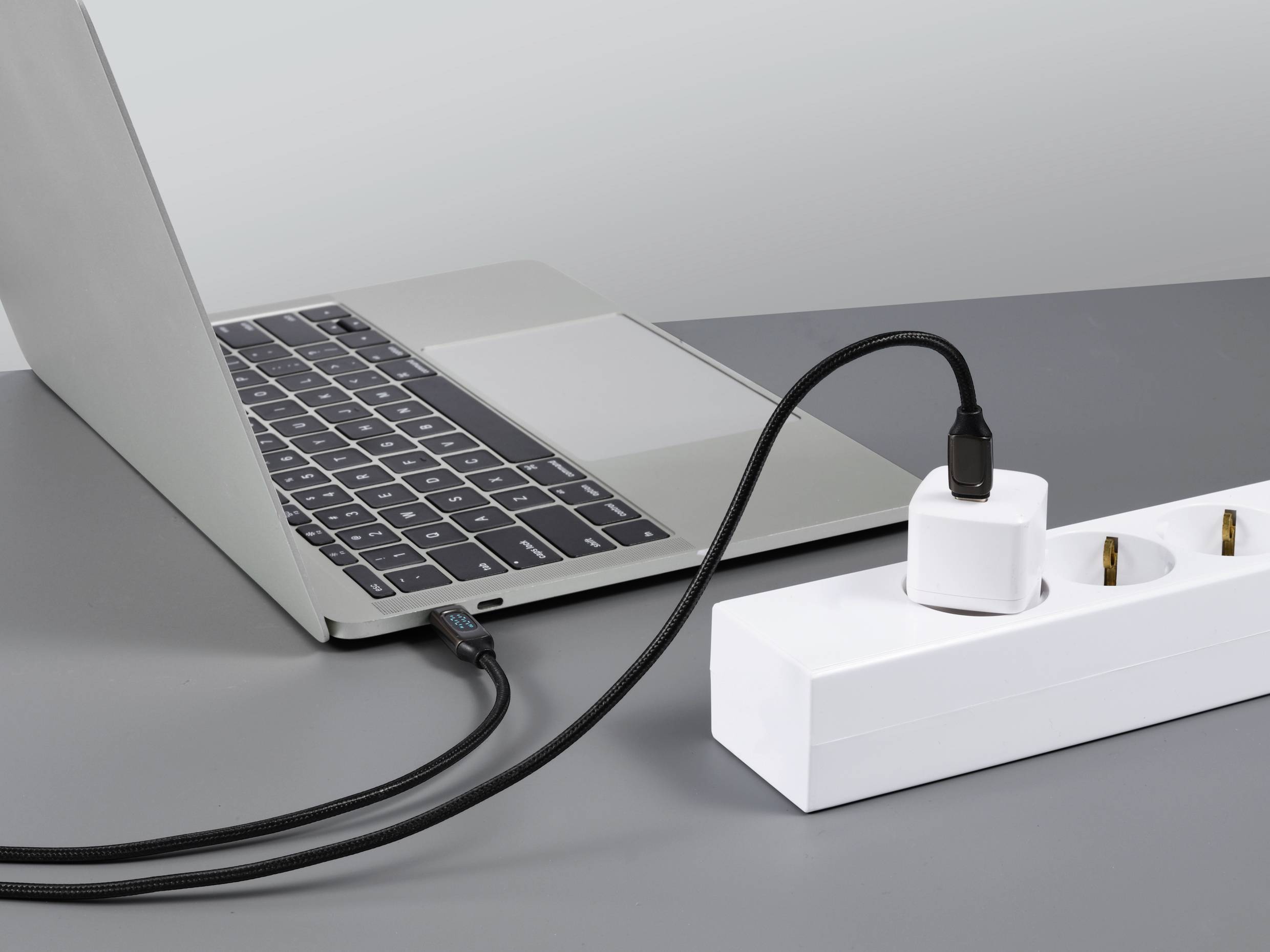 Ein Laptop ist über ein USB-Kabel mit einem Adapter an eine Steckdosenleiste angeschlossen und wird geladen.