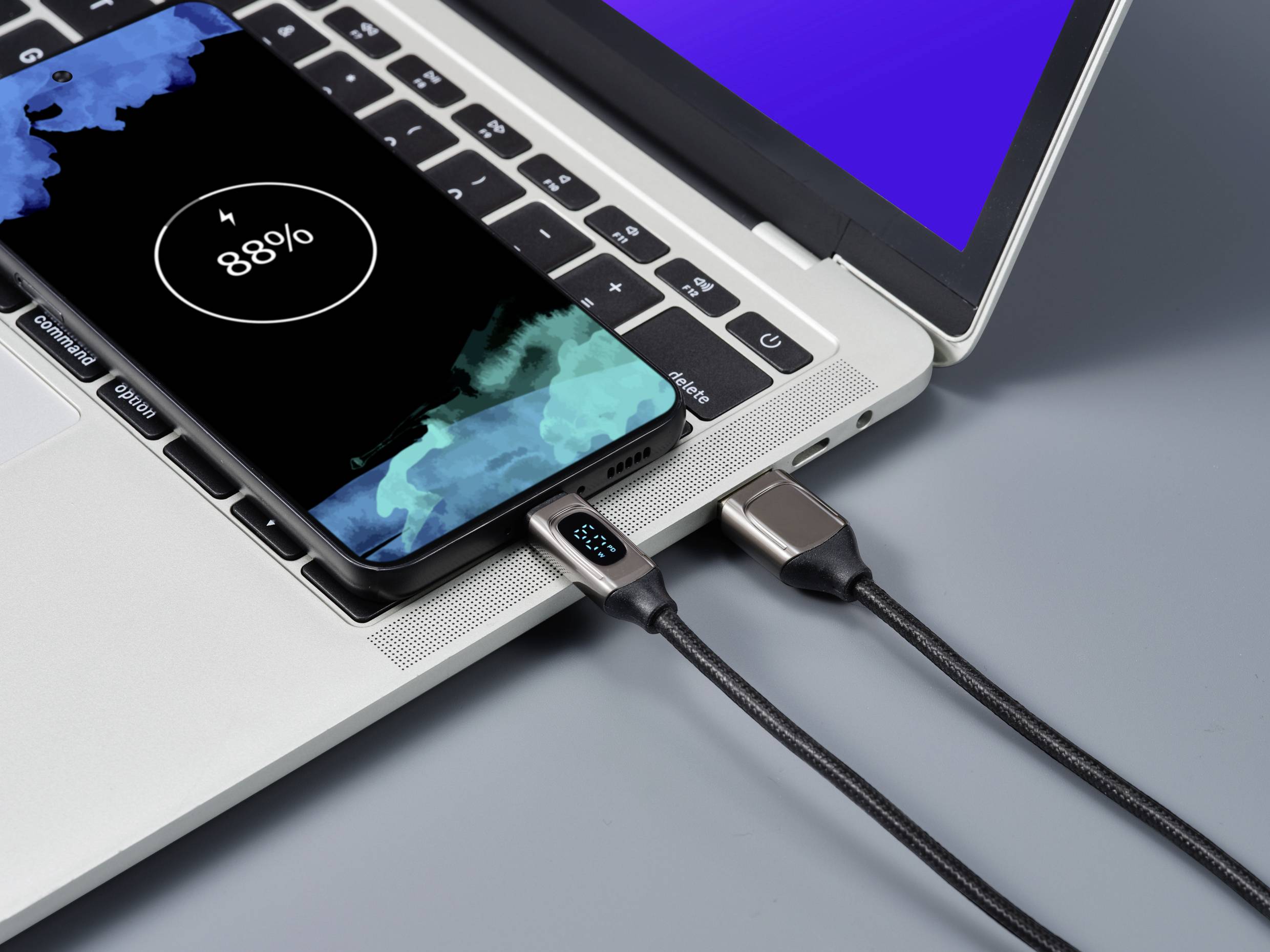 Ein Smartphone lädt auf einem Laptop. Das Display zeigt '88%' an. Ein Ladekabel verbindet das Telefon mit dem Laptop, der Bildschirm ist blau.