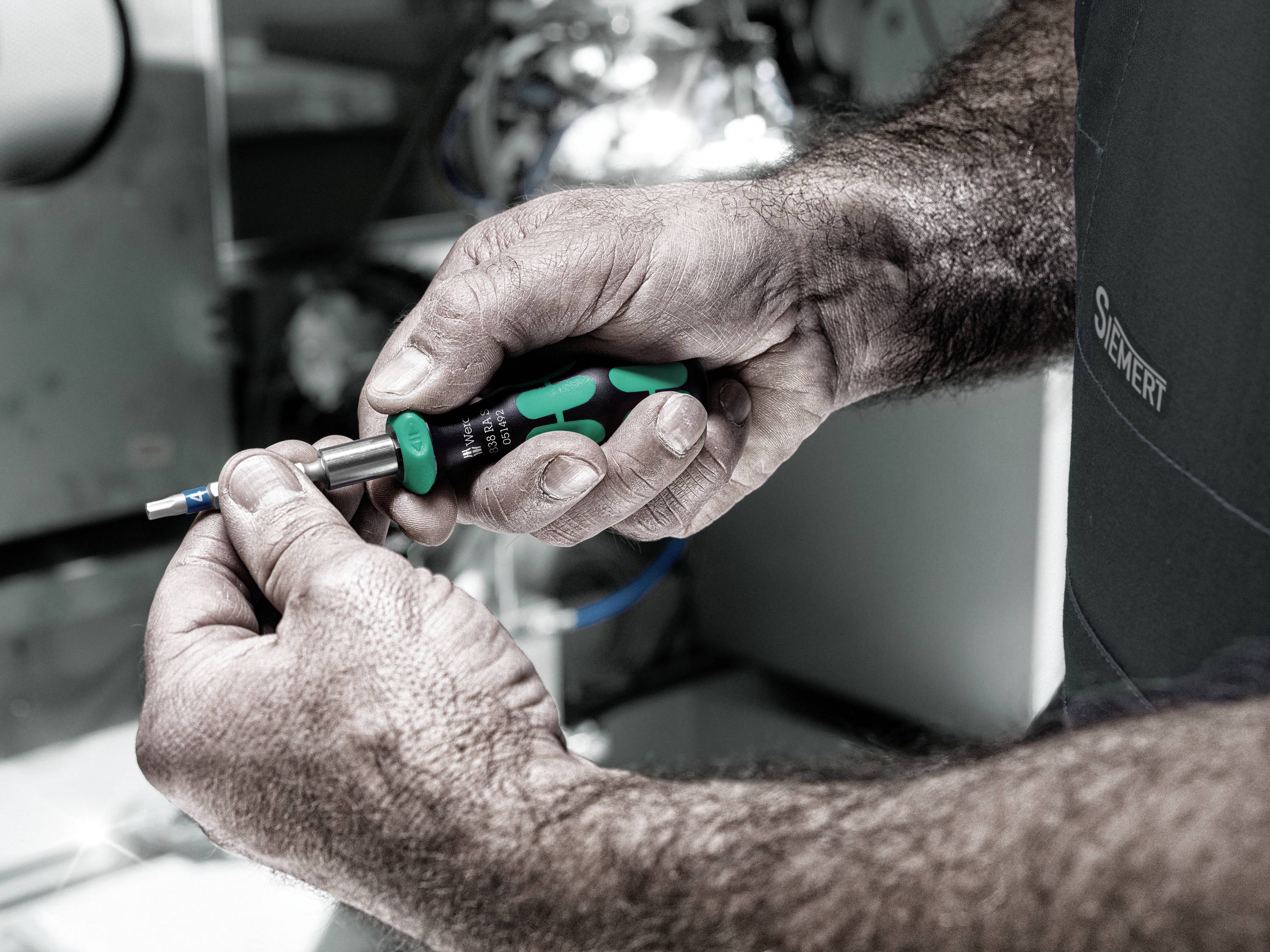 Nahaufnahme von Händen eines Technikers, der einen Schraubendreher hält und an einer Metallmaschine arbeitet.