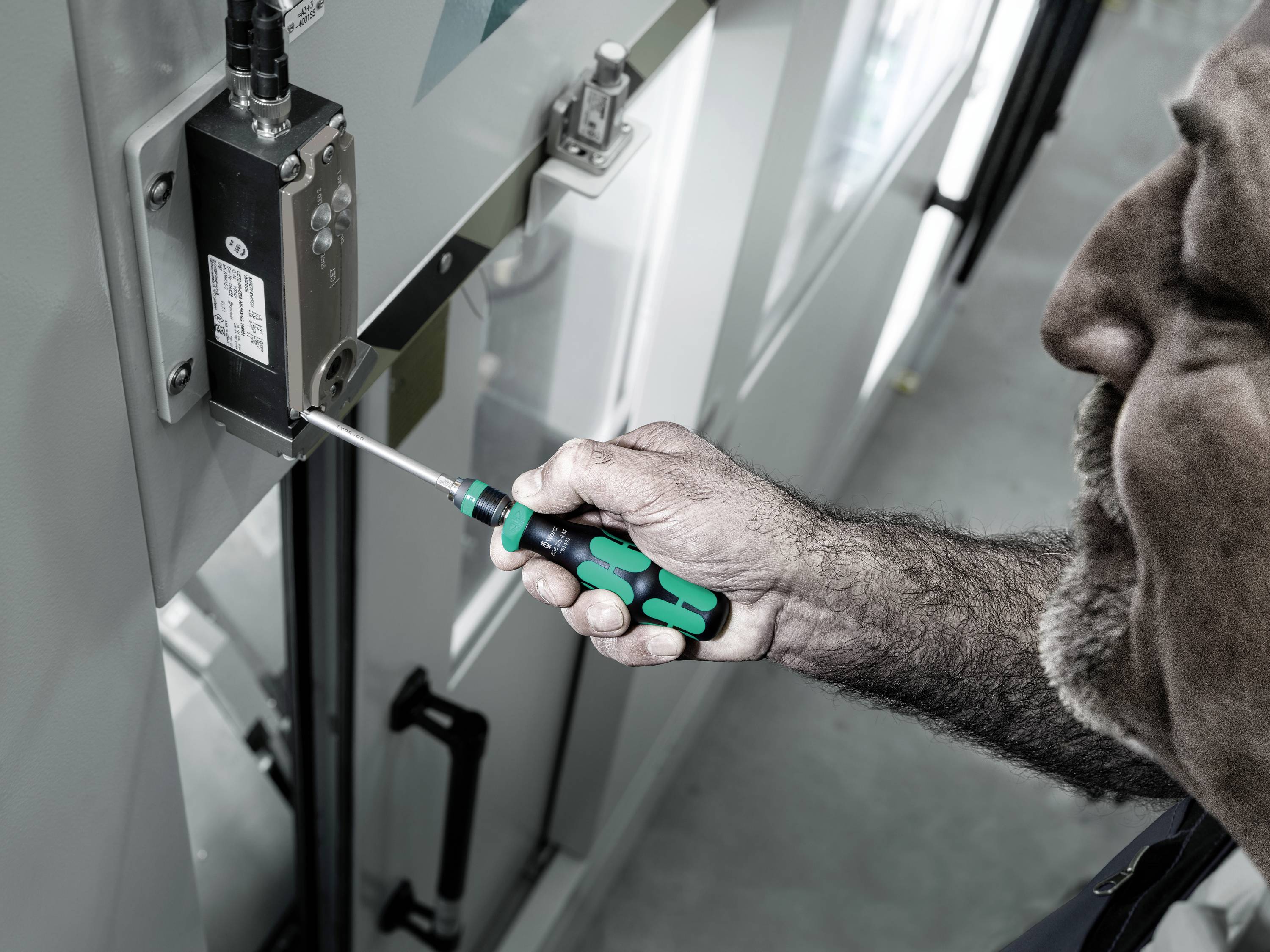 Ein Mann repariert eine Maschine mit einem Schraubendreher. Nahaufnahme zeigt präzise Tätigkeit an einem elektronischen Bauteil.