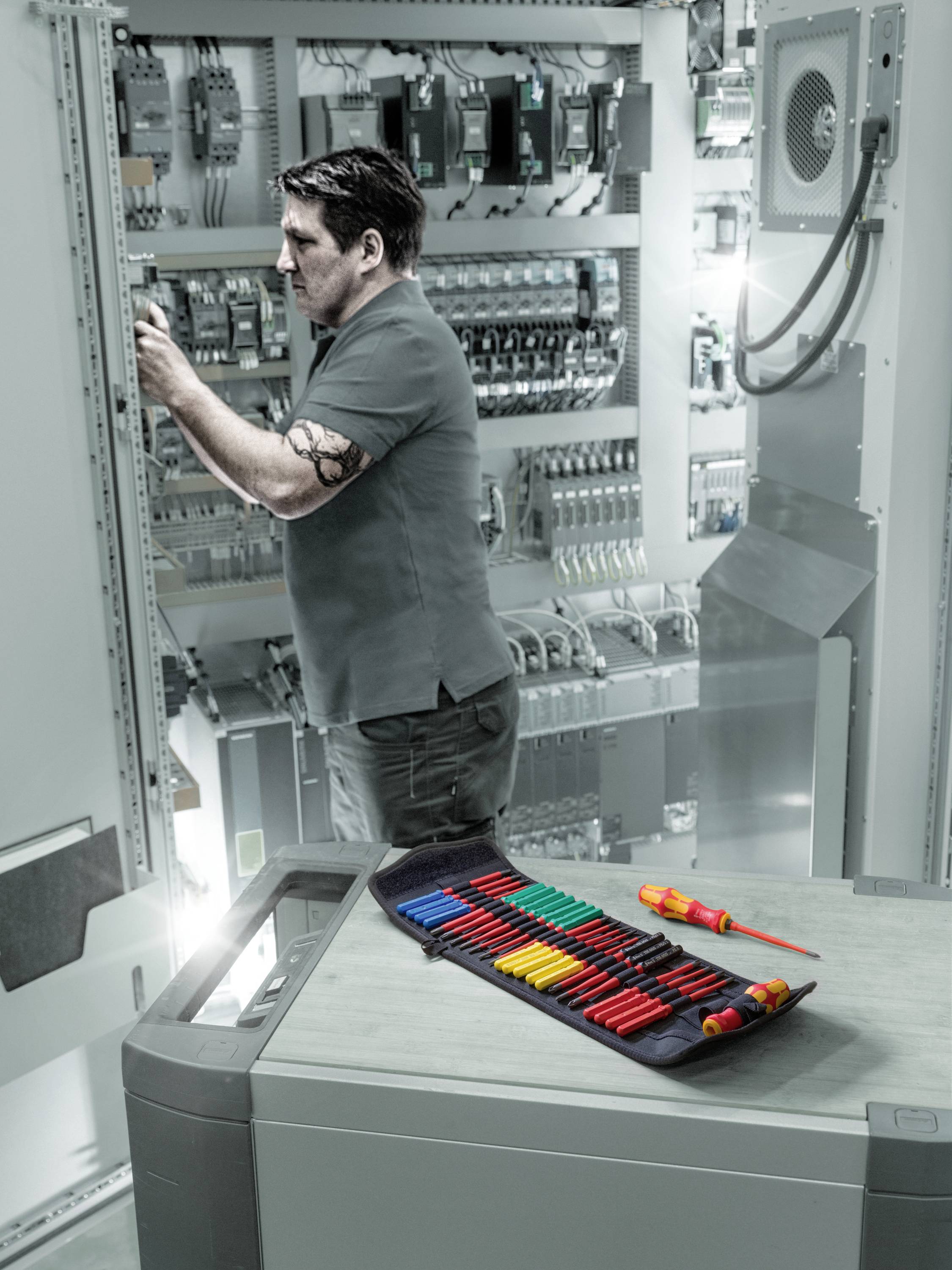 Ein Techniker arbeitet an einem Schaltschrank in einer industriellen Umgebung. Im Vordergrund liegt ein offenes Etui mit Werkzeugen.