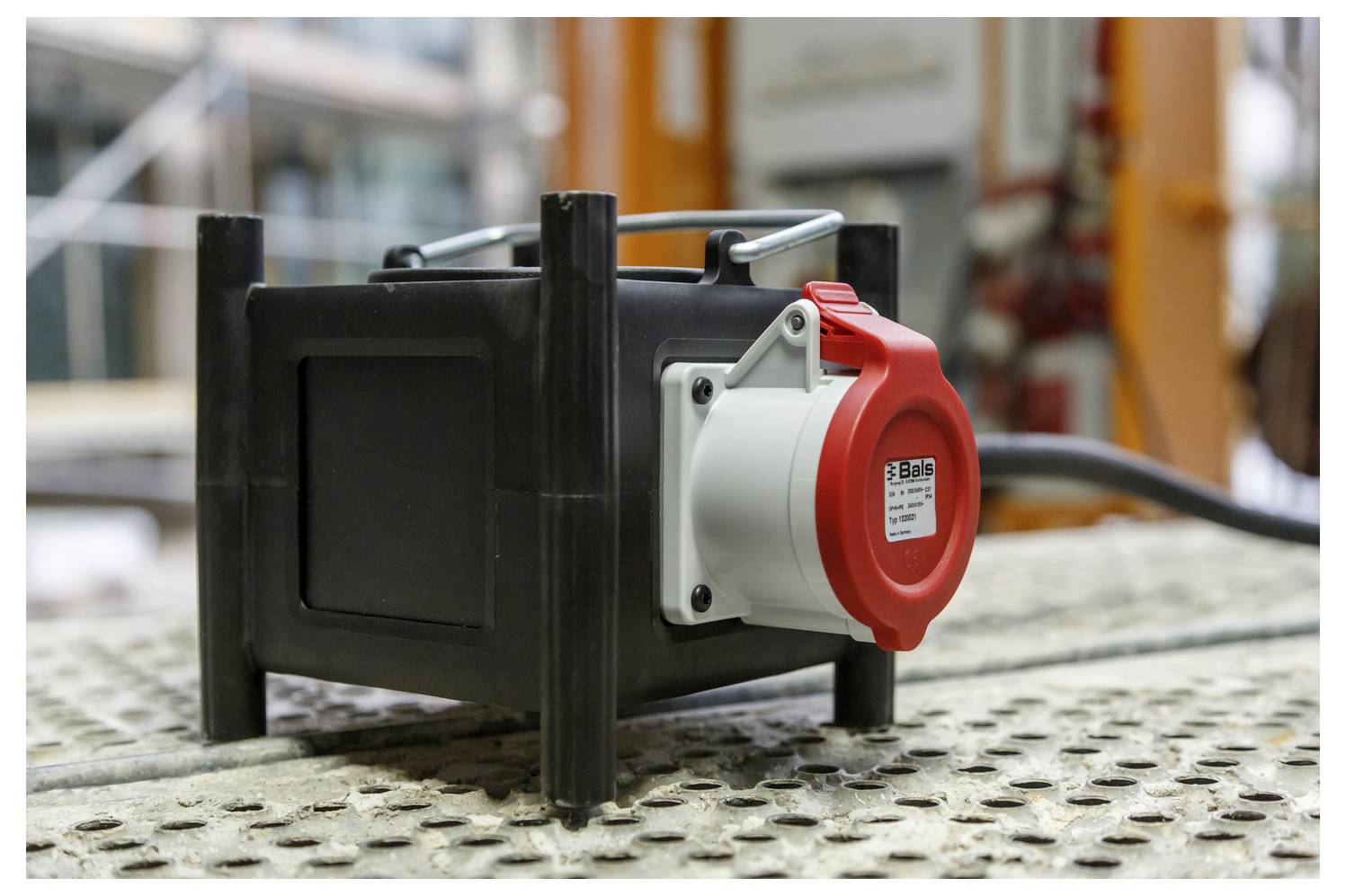 Tragbare schwarze Elektrosteckdosenbox mit einer roten Industriesteckdose auf einer Werkbank oder Baustelle.