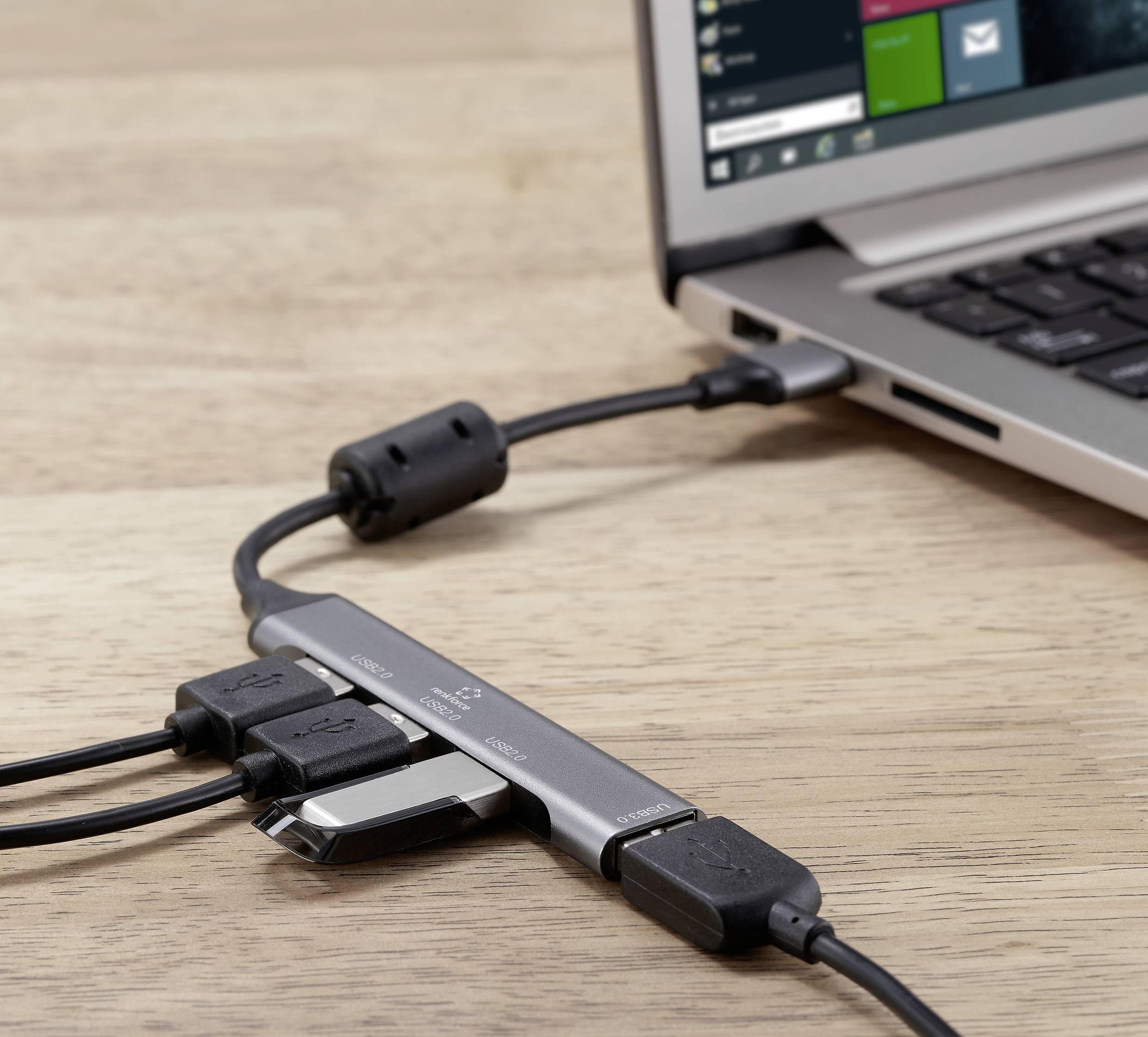 Ein Laptop ist mit mehreren USB-Geräten über einen USB-Hub verbunden. Der Hub liegt auf einem Holztisch, das Laptop ist teilweise sichtbar.