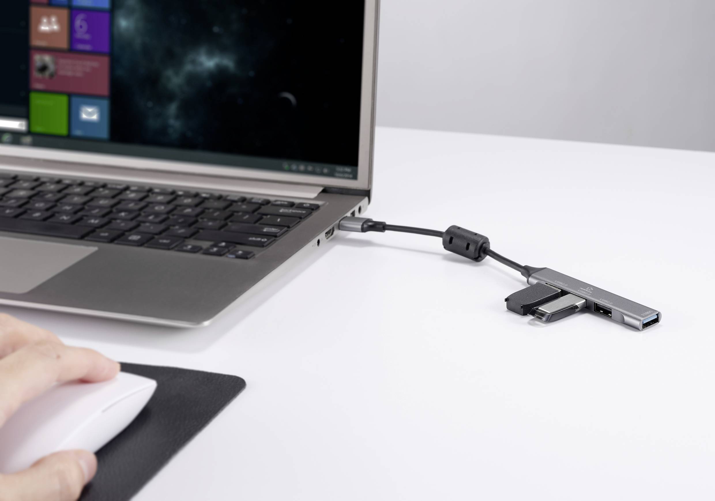 Ein Laptop mit offenem Bildschirm ist auf einem Tisch. Ein USB-Hub ist an den Laptop angeschlossen. Eine Hand benutzt eine Computermaus.