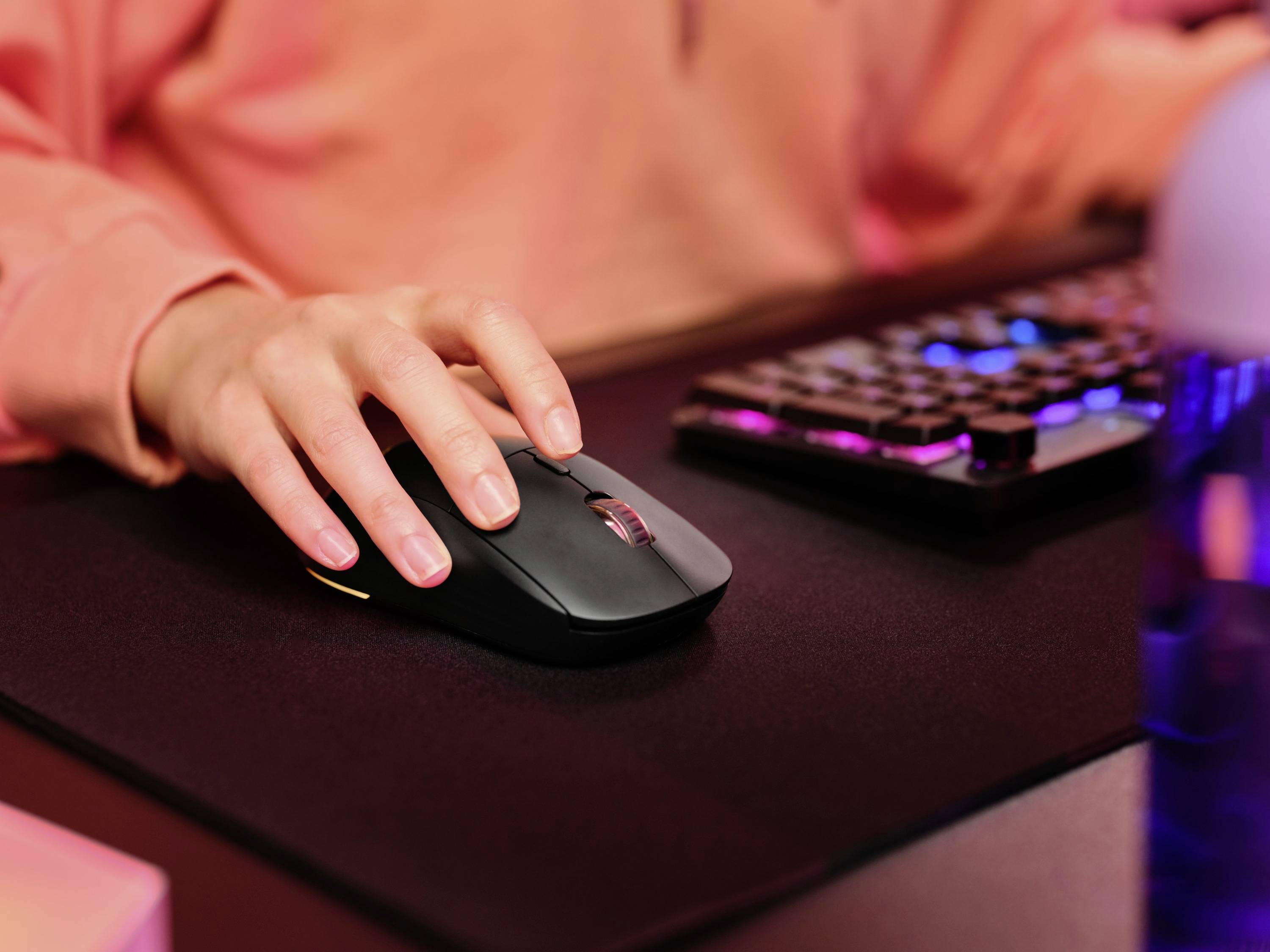 Eine Person benutzt eine Computermaus auf einem Schreibtisch, neben einer beleuchteten Tastatur.