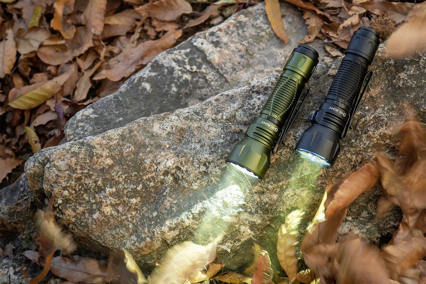 Zwei Taschenlampen leuchten auf einem Felsen, umgeben von Herbstblättern. Eine ist olivgrün, die andere schwarz.
