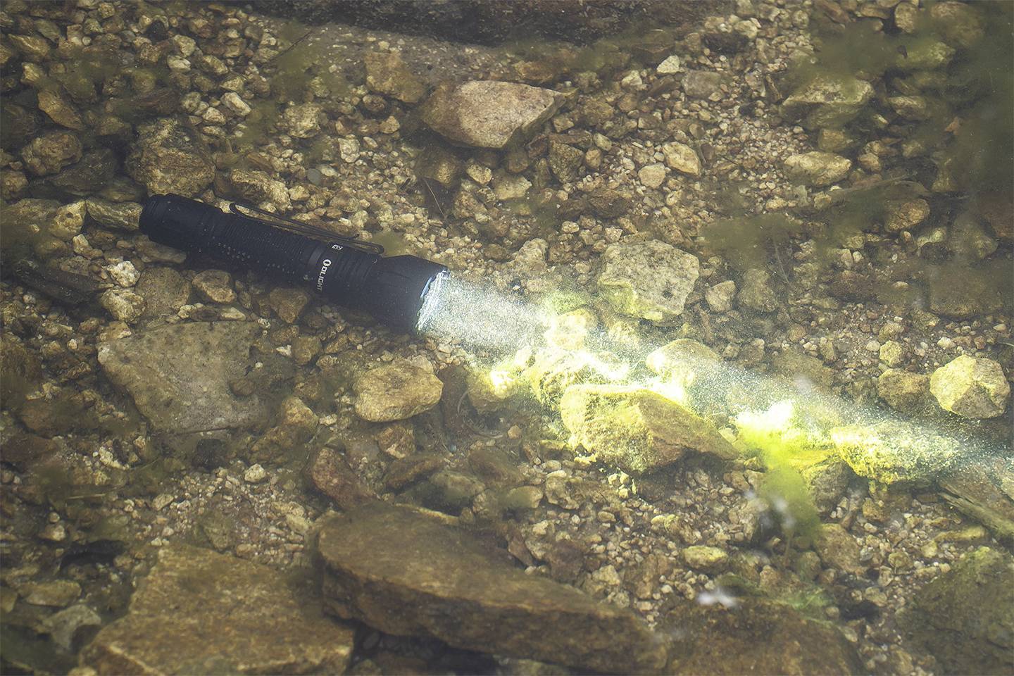 Taschenlampe unter Wasser, deren Lichtstrahl auf den steinigen Boden leuchtet.