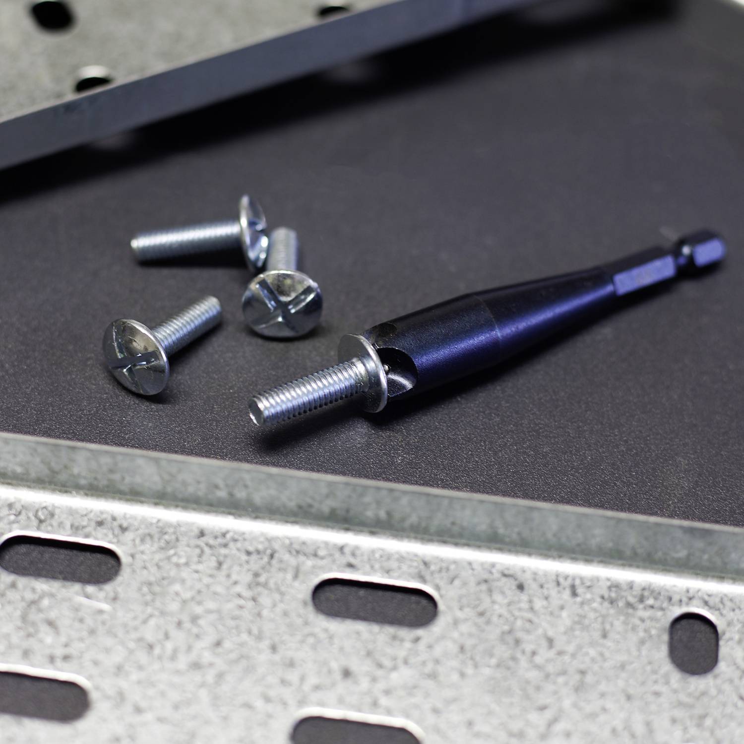 Mehrere Metallschrauben und ein Bohrer liegen auf einer Metalloberfläche mit Löchern.