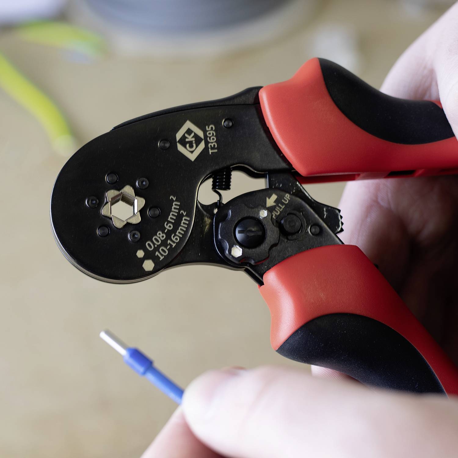 Eine Hand hält eine rote Crimpzange, die an einem blauen Kabel arbeitet.