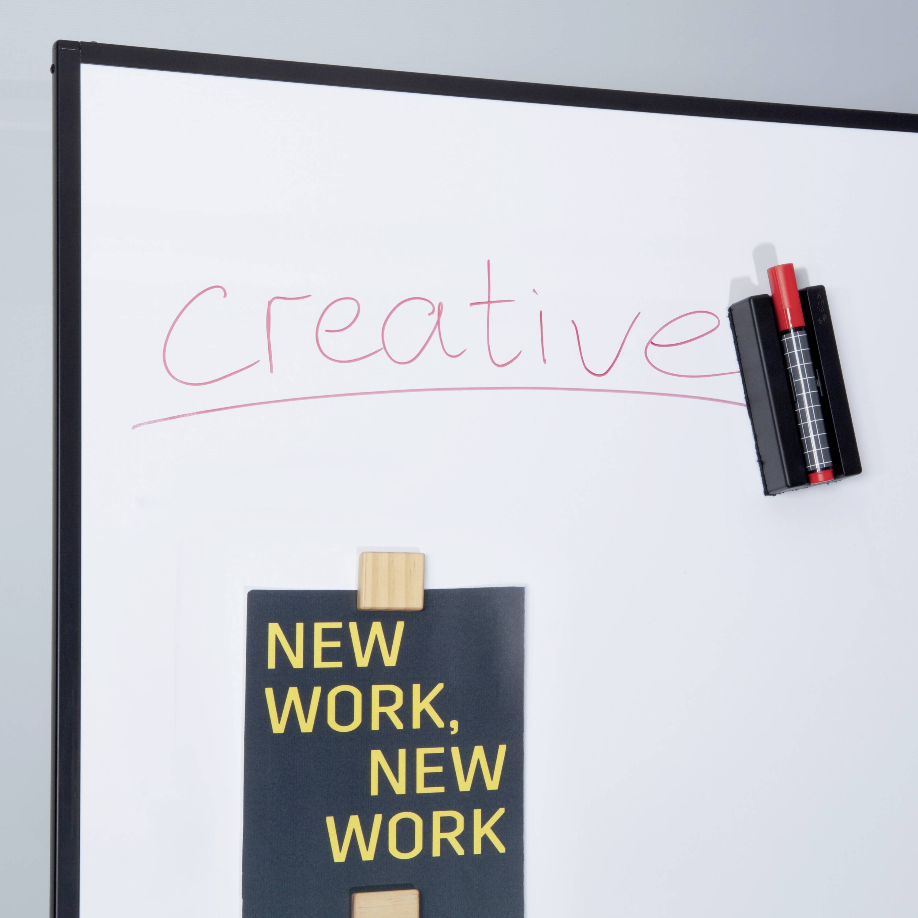 Ein Whiteboard mit der Aufschrift 'Creative'. Darunter ein kleines Plakat mit den Worten 'New Work, New Work' und Stiftehalter oben rechts.