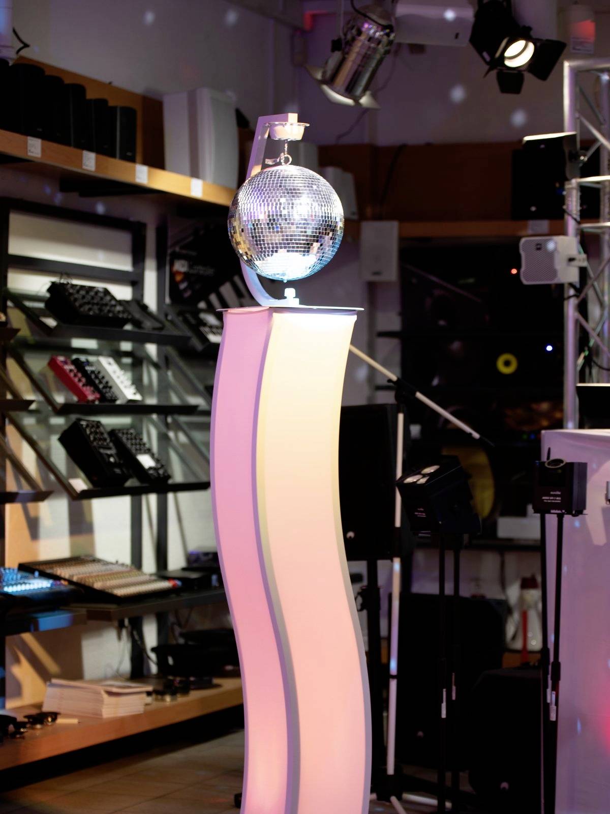 Ein beleuchteter Podest in einem Musikgeschäft zeigt eine glänzende Discokugel. Im Hintergrund sind Musikinstrumente und Lautsprecher sichtbar.
