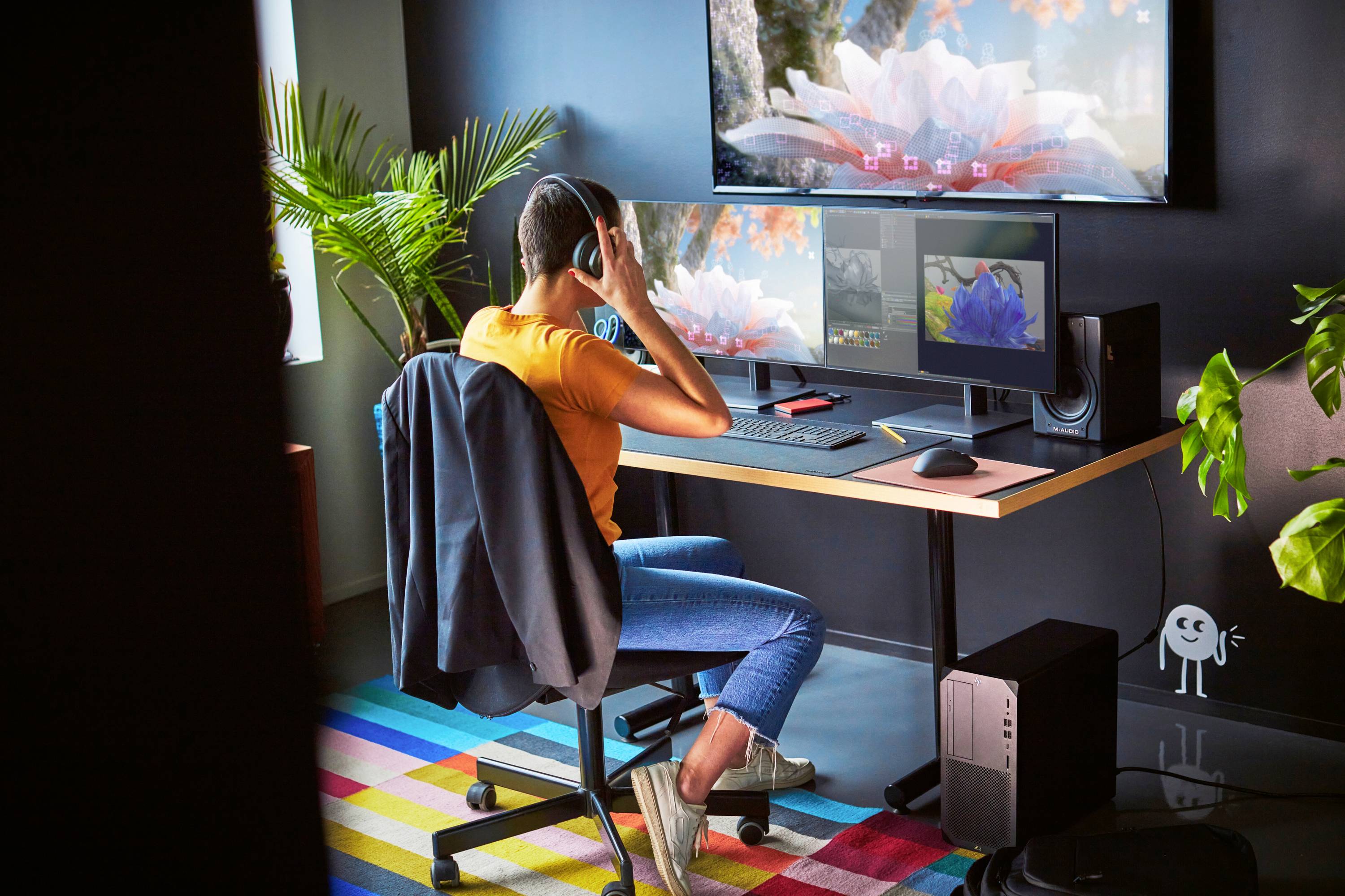 Eine Person sitzt an einem Schreibtisch mit drei Bildschirmen, trägt Kopfhörer und arbeitet in einem modern eingerichteten Büro.