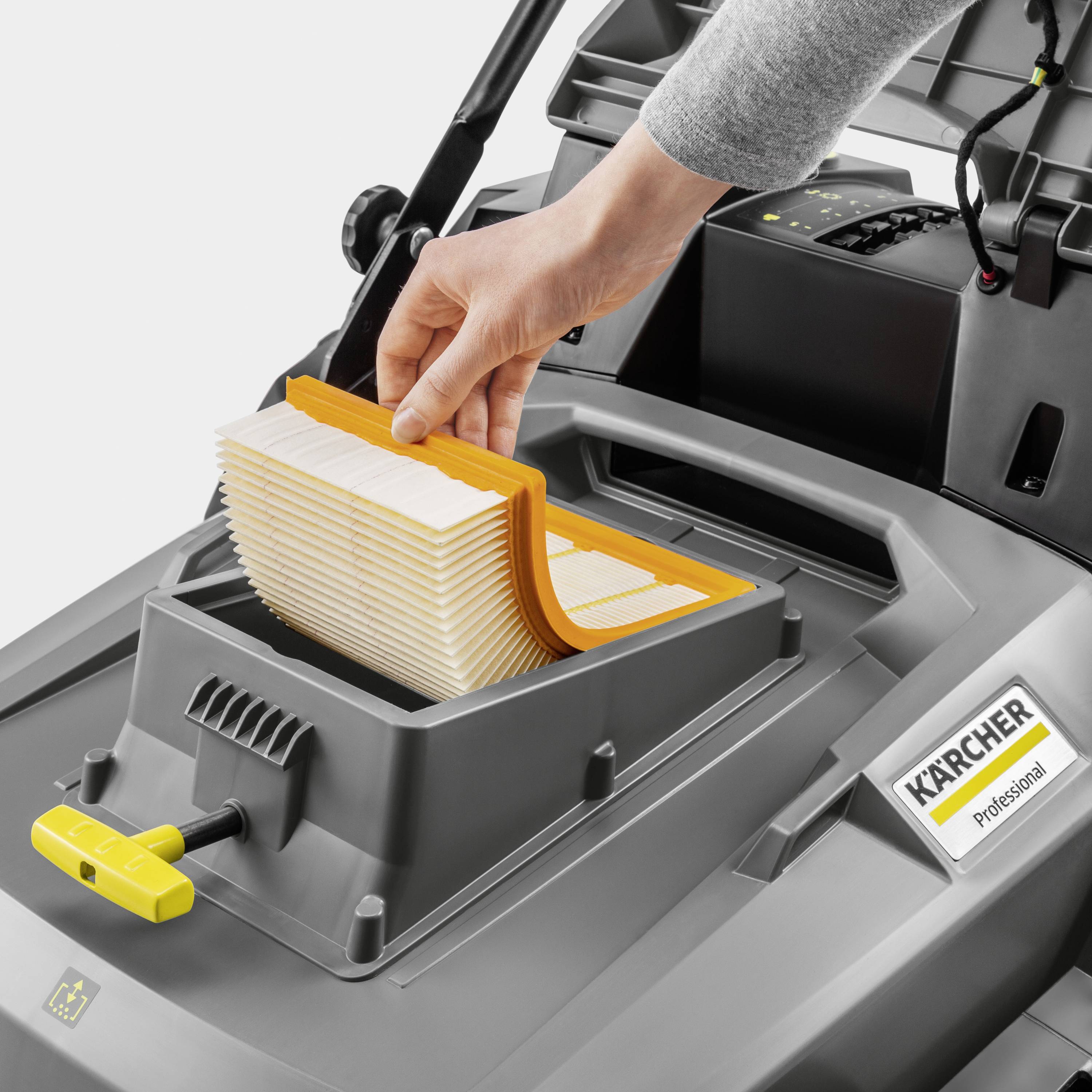 Eine Hand setzt einen rechteckigen Filter in einen grauen Industriestaubsauger ein, mit dem Logo 'Kärcher Professional' daneben.