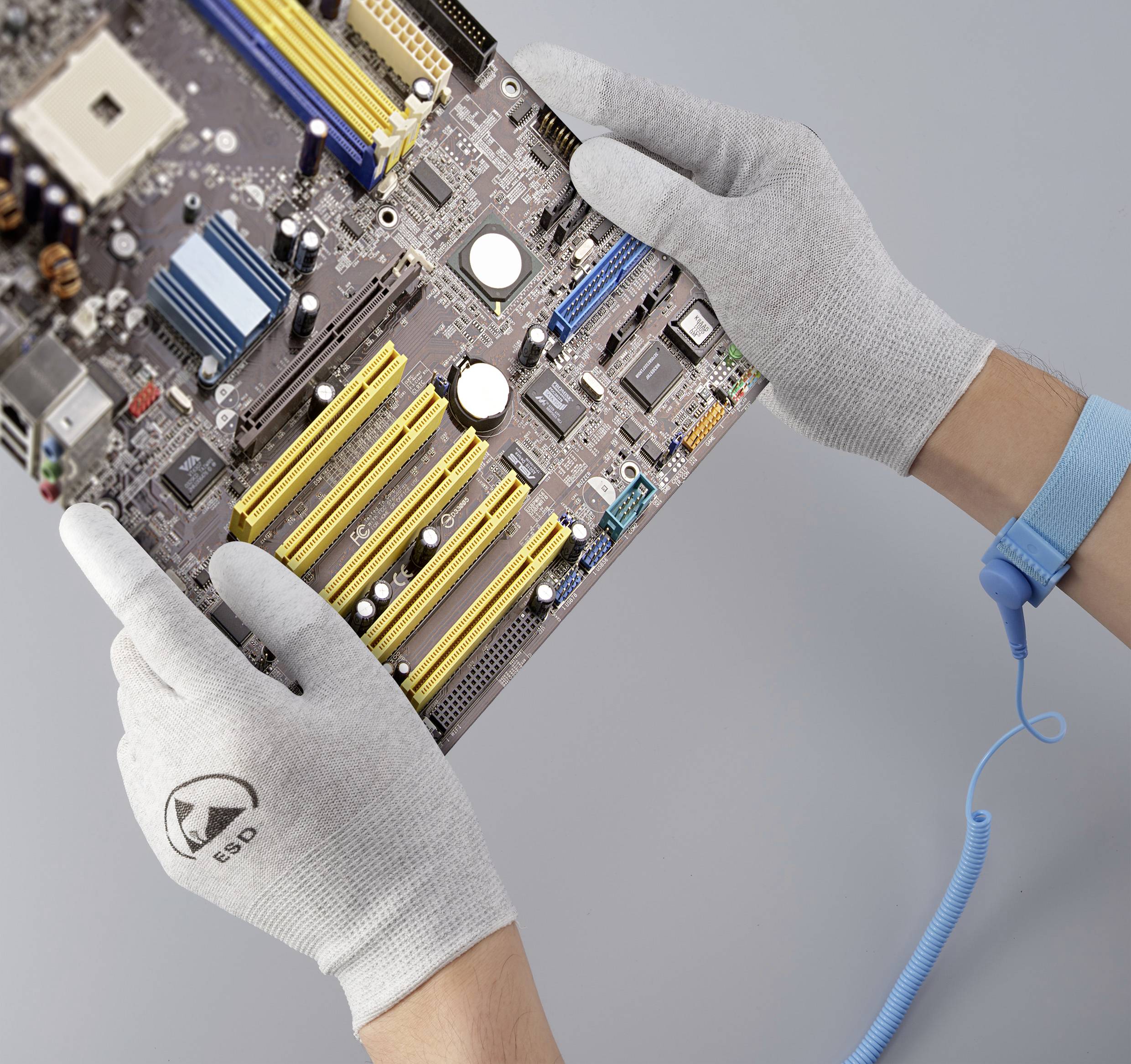 Ein Paar Hände in ESD-Handschuhen hält eine Computerplatine, während eine elektrostatische Schutzmanschette um das Handgelenk getragen wird.