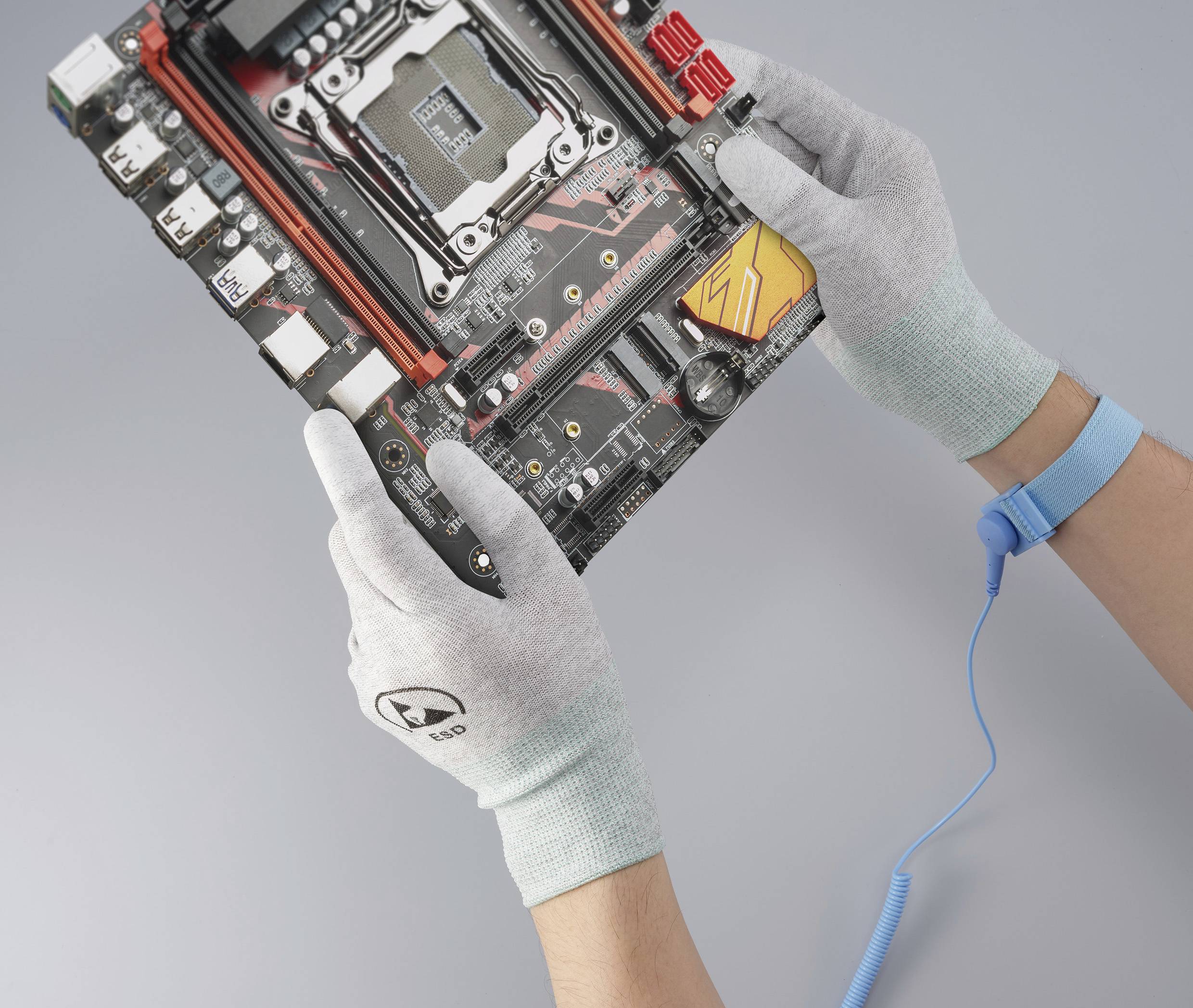 Zwei behandschuhte Hände halten eine Computer-Mainboard-Platine mit sichtbarem CPU-Sockel und Schaltkreisen. Ein Erdungskabel ist am Handgelenk befestigt.