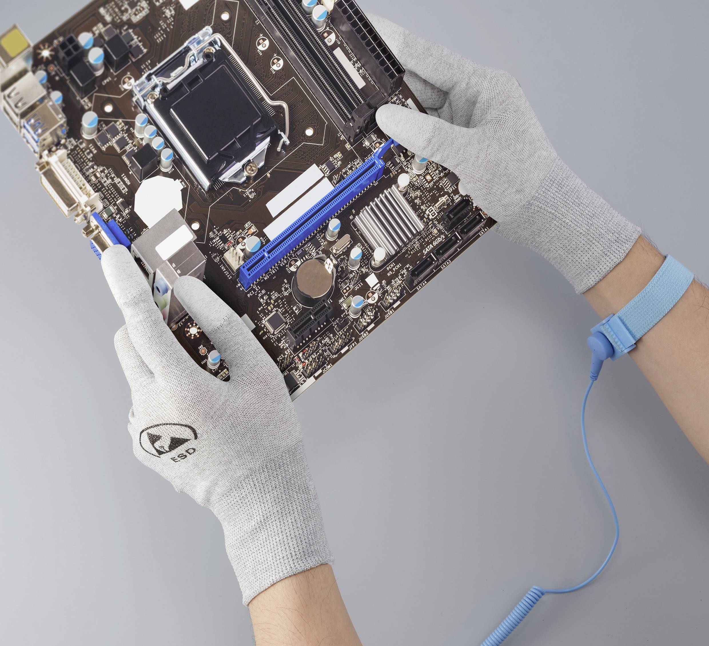Zwei Hände mit grauen Handschuhen halten eine Computerhauptplatine über einer grauen Fläche.