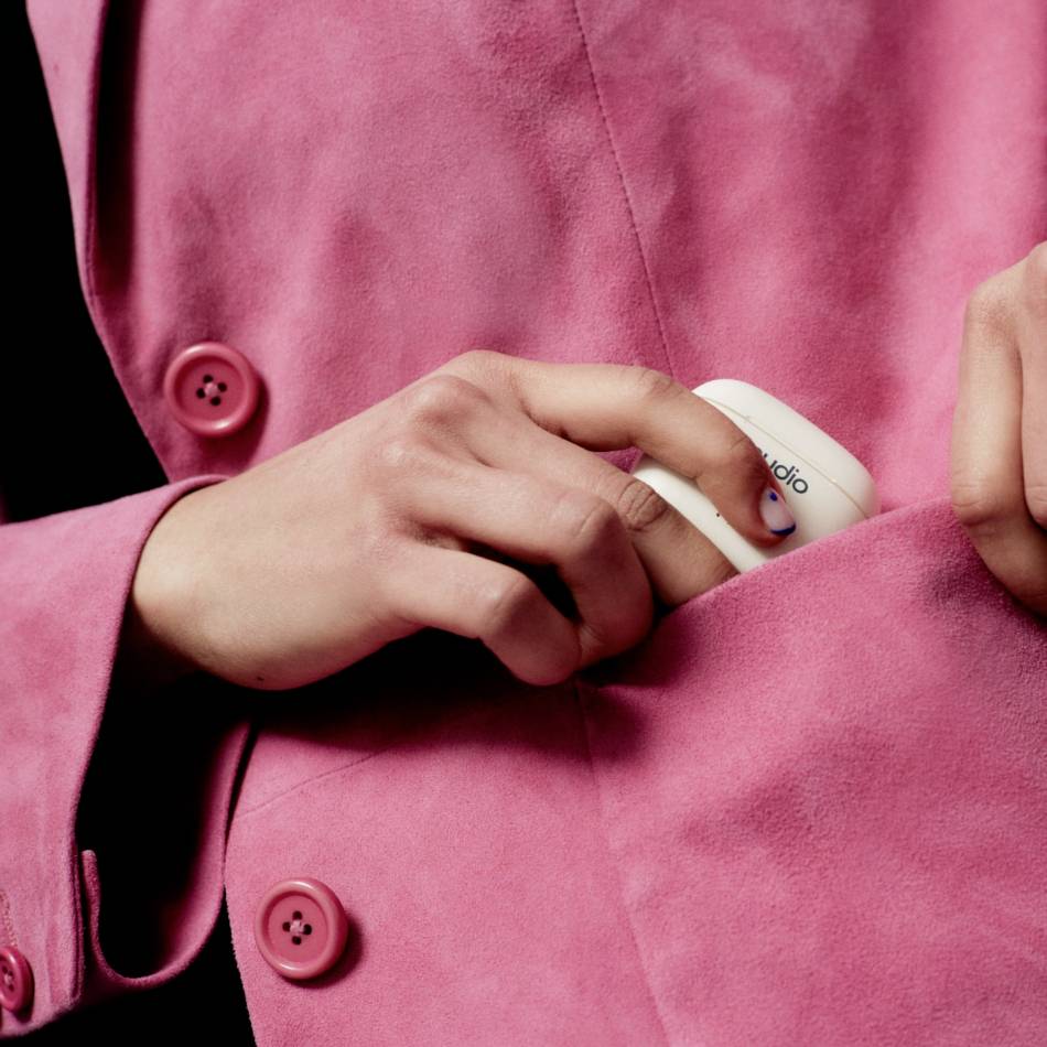 Eine Person steckt ein weißes Gerät in die Innentasche eines pinken Mantels. Das Gerät trägt die Aufschrift 'studio'.