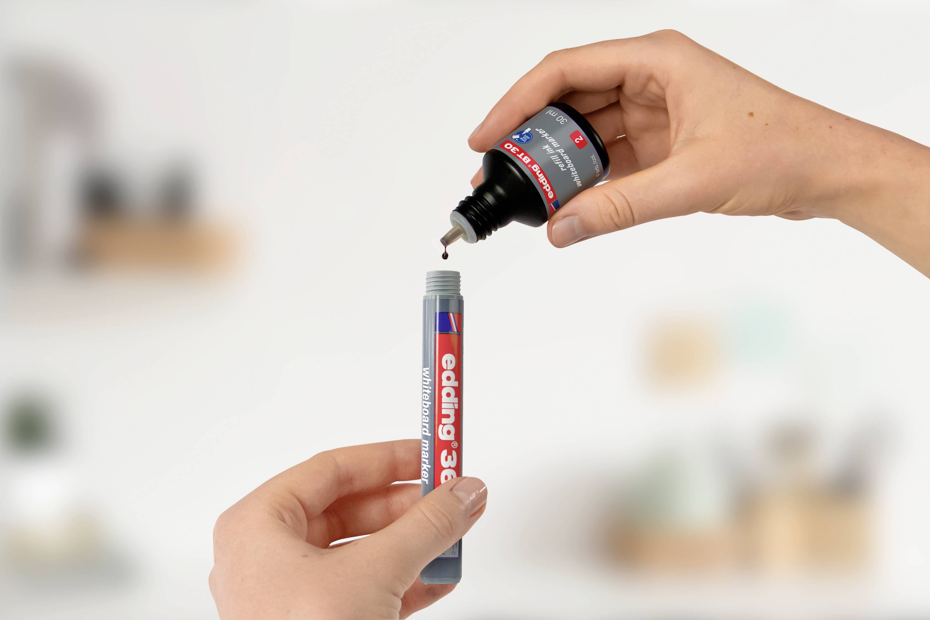 Zwei Hände bei der Nachfüllung eines edding 3000 Markers mit Tinte. Eine Hand hält den Marker, die andere fügt die Tinte hinzu.
