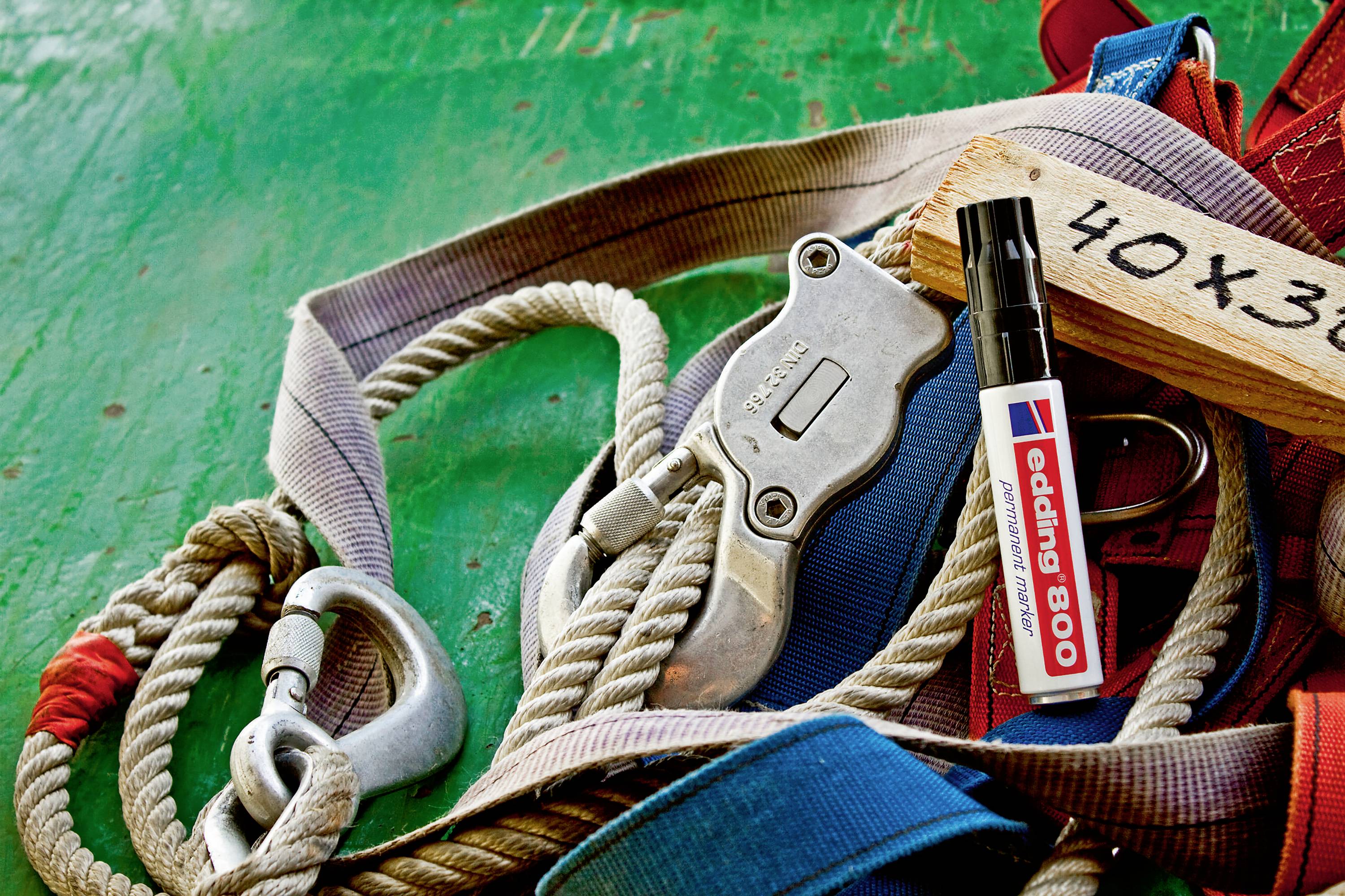 Bergsteiger-Ausrüstung: Seil, Karabiner, Klettergurt und Edding 800 Marker liegen auf grünem Untergrund nebeneinander.