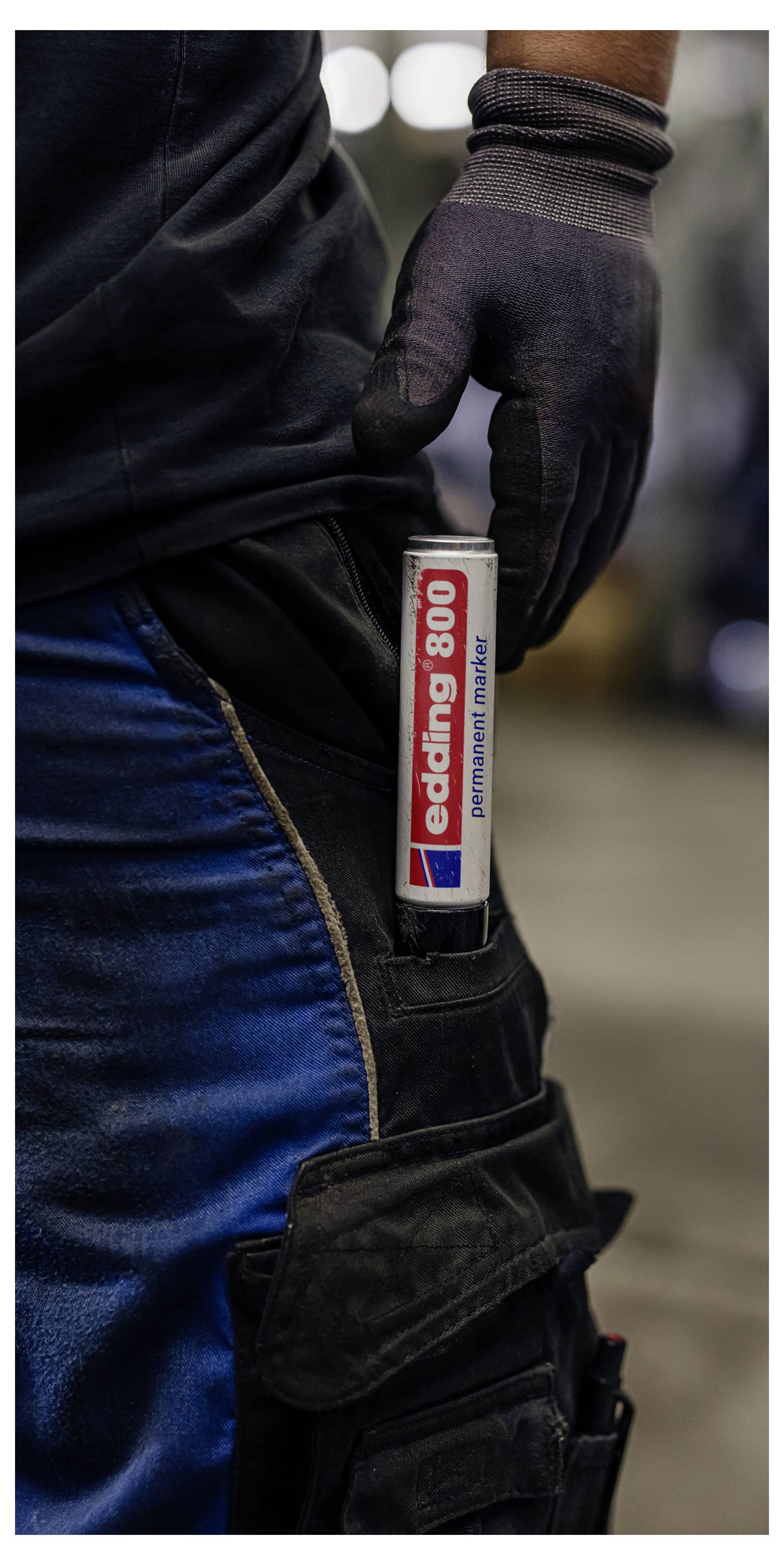 Nahaufnahme einer handschuhtragenden Person mit einem weißen Edding-800-Permanentmarker, der in einer schwarzen Werkzeugtasche an der Hose befestigt ist.