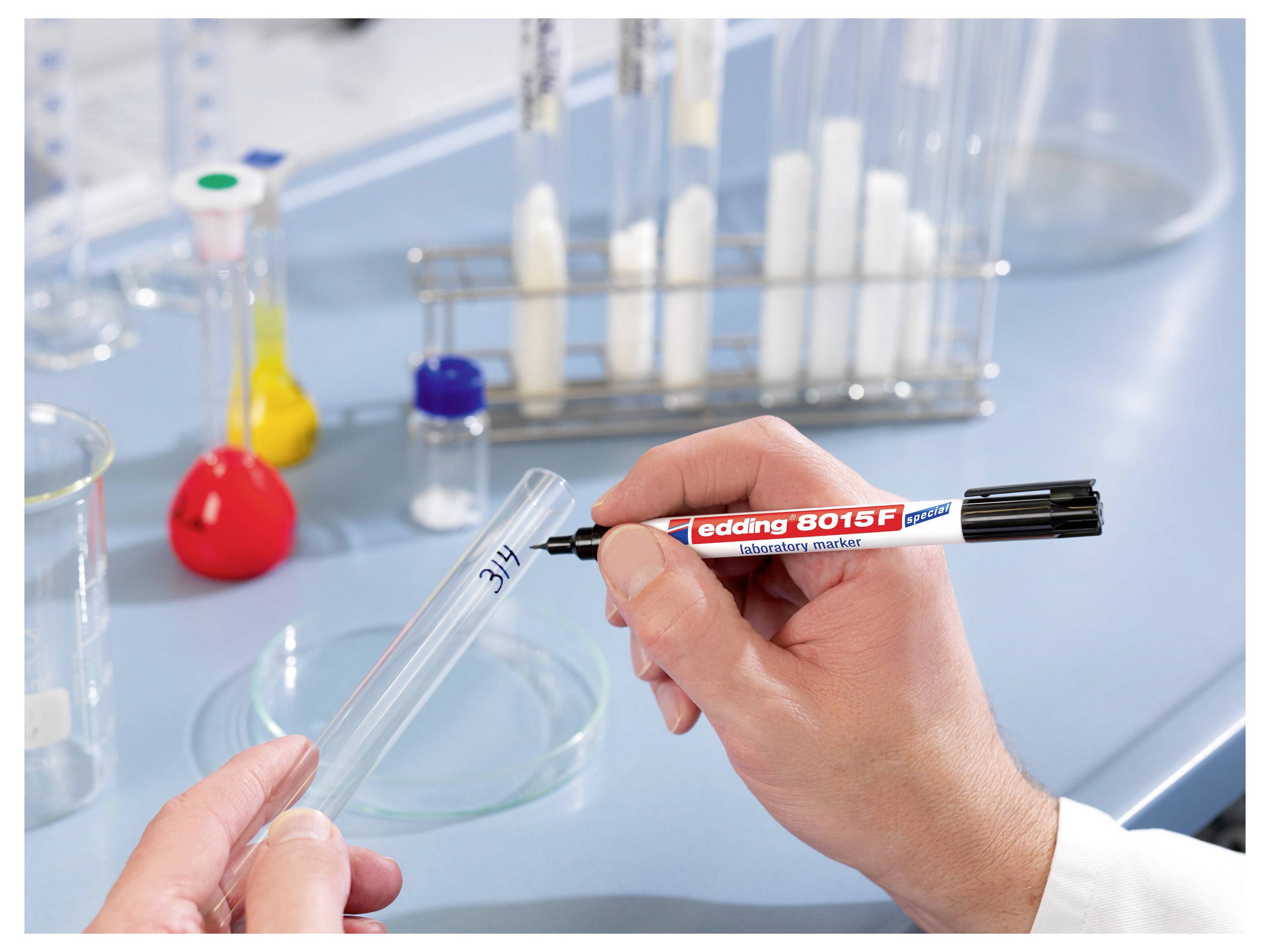 Beschriftung eines Reagenzglases mit einem schwarzen Permanentmarker in einem Labor, mit Glaswaren und Laborausrüstung im Hintergrund.