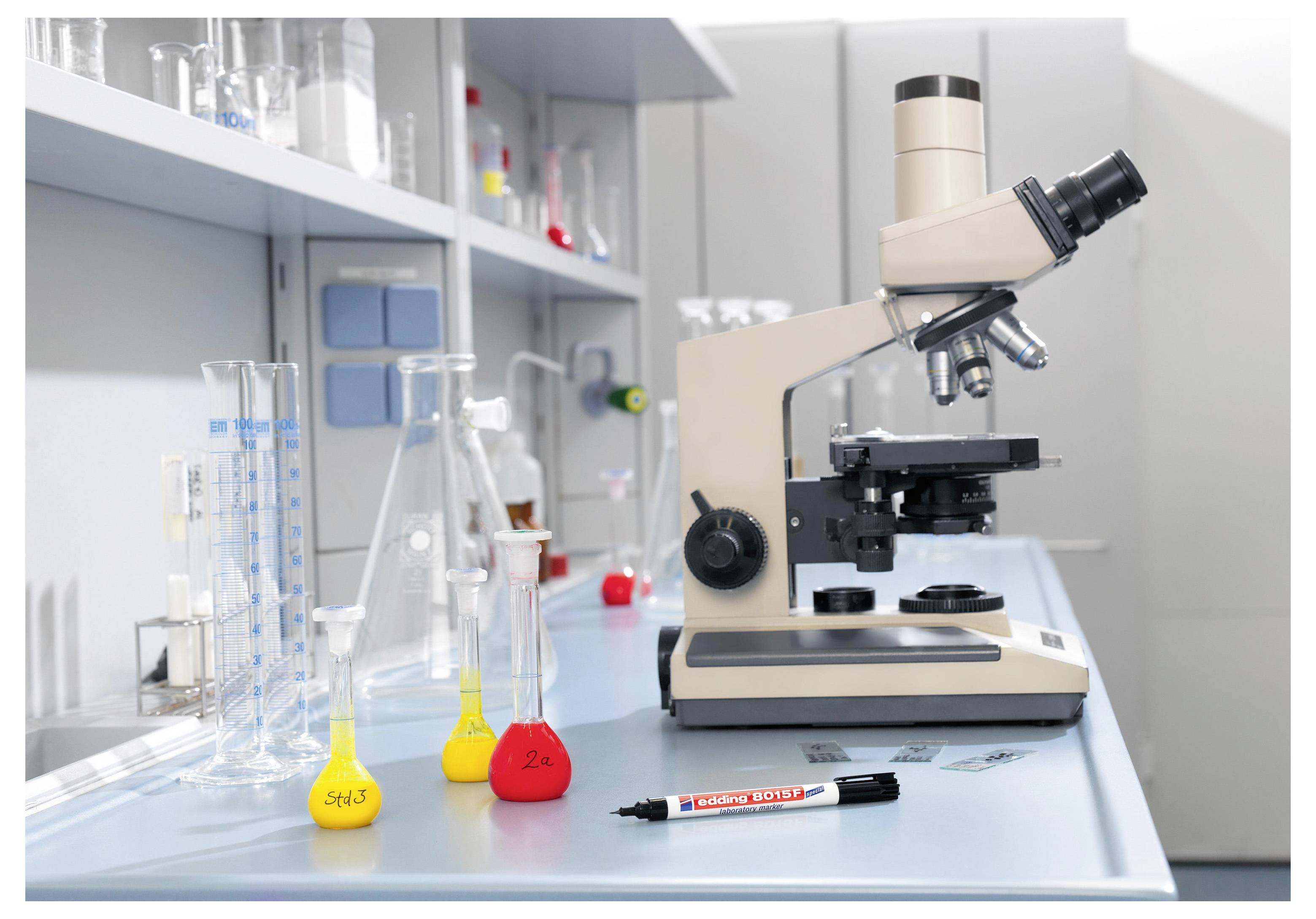 Labormikroskop neben Glaspechern und farbgefüllten Flaschen auf einer Laborbench