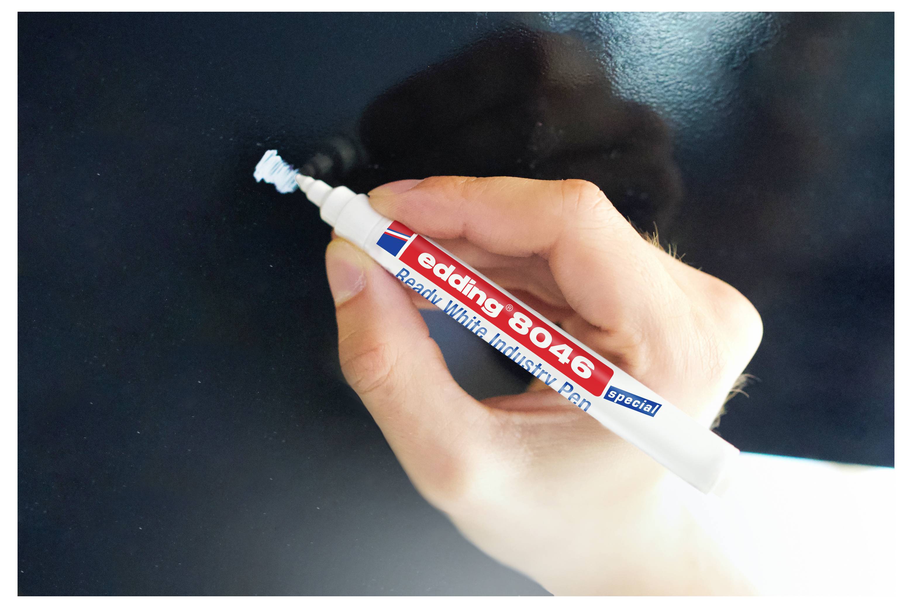 Hand, die einen weißen Edding 8046 Whiteboard-Lackmarker mit blauer Keilspitze über einer dunklen Oberfläche hält.