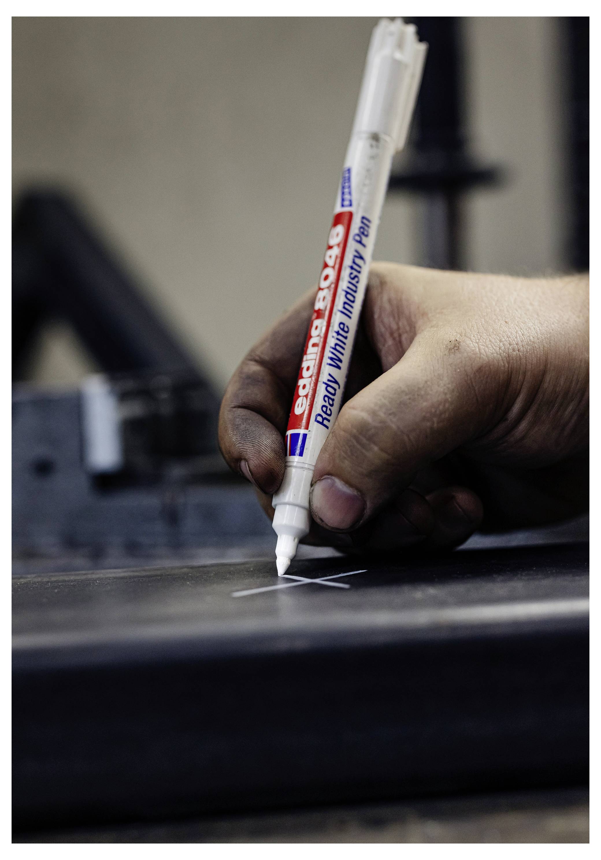 Nahaufnahme einer Hand, die einen weißen Industriemarker verwendet, um eine weiße Linie auf einer dunklen Oberfläche zu zeichnen.