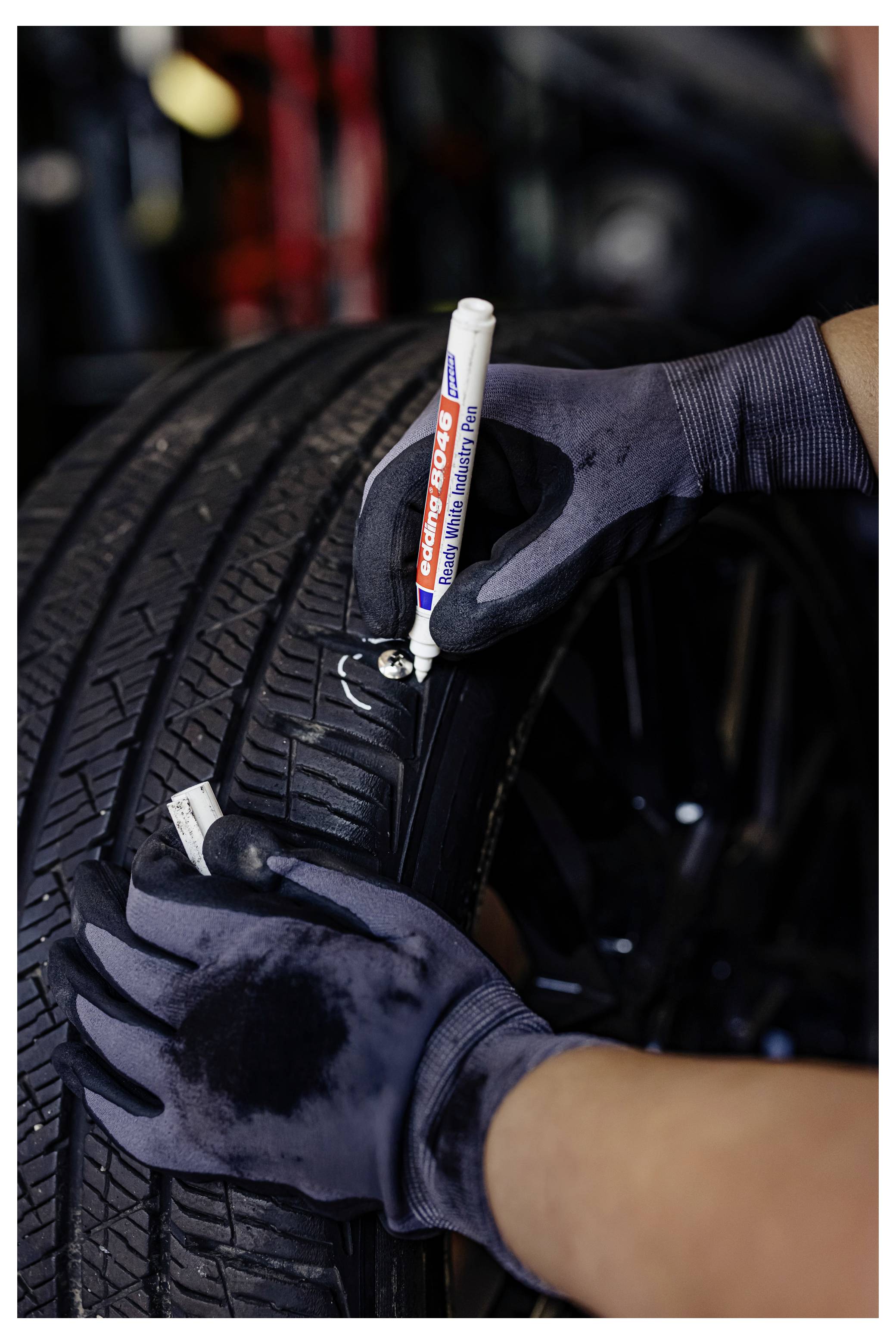 Behandschuhte Hände, die eine Reifenflanke mit einem weißen Lackstift während einer Reifenprüfung oder Reparatur markieren.
