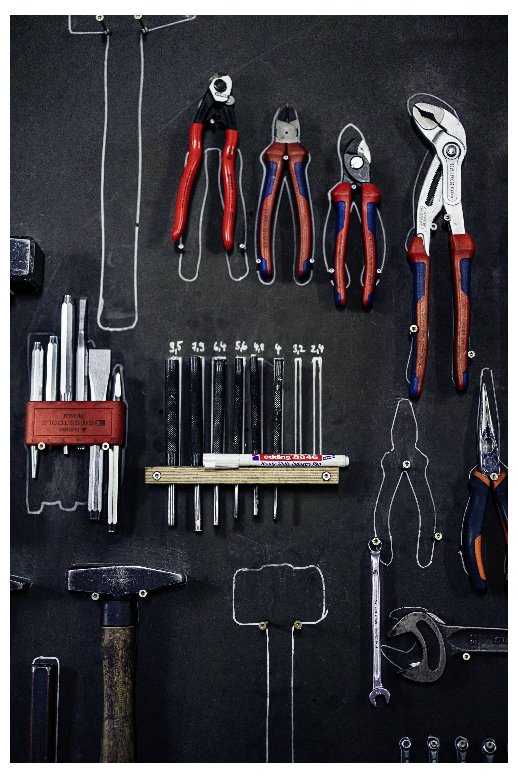 Sortierte Handwerkzeuge ordentlich auf einer dunklen Wand oder Platte angeordnet, einschließlich Zangen, Schraubenschlüssel, eines Hammers und Schraubendrehern.