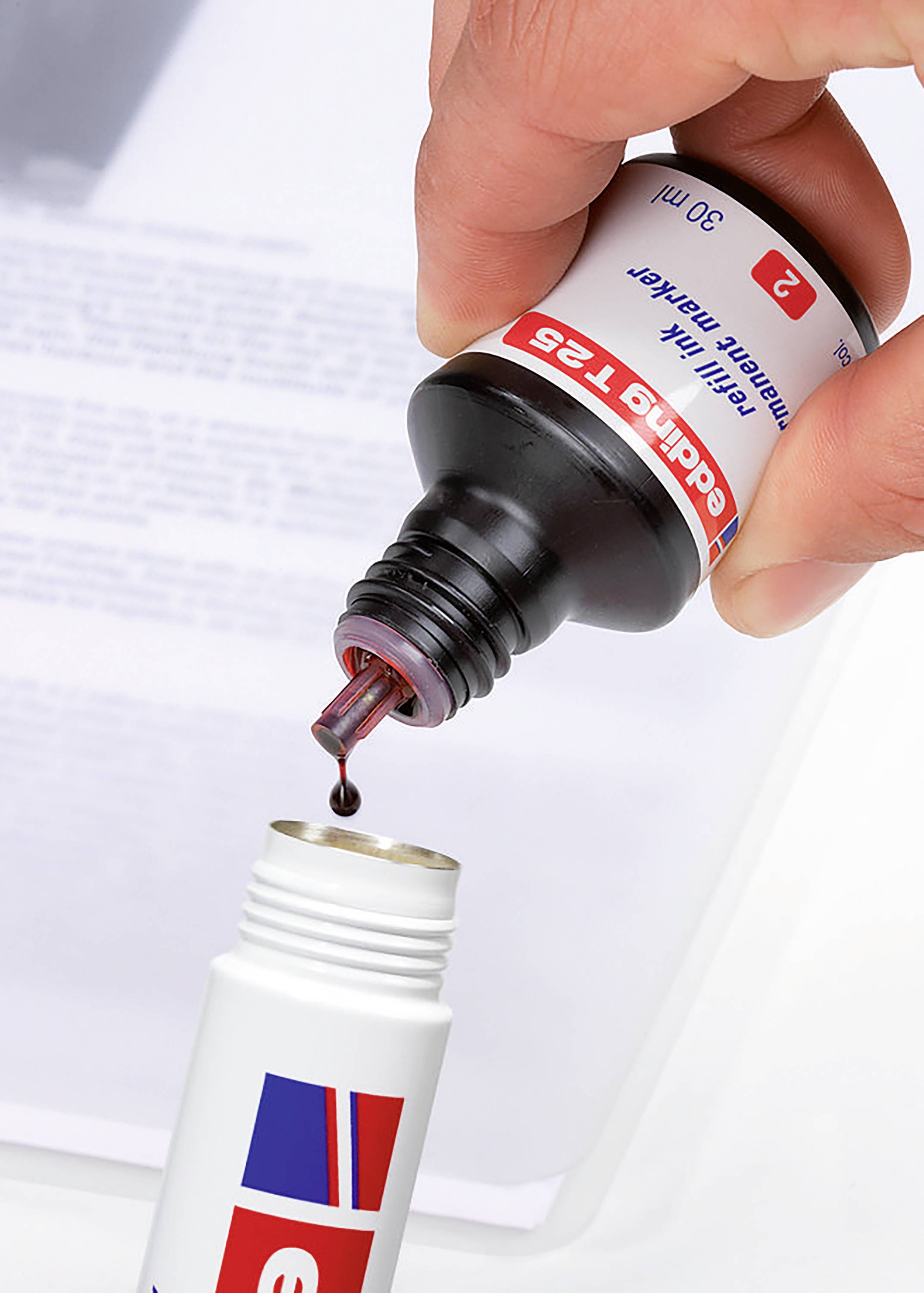 Eine Hand füllt eine kleine Flasche mit roter Flüssigkeit aus einer Tropfflasche. Im Hintergrund ist ein verschwommenes Dokument erkennbar.