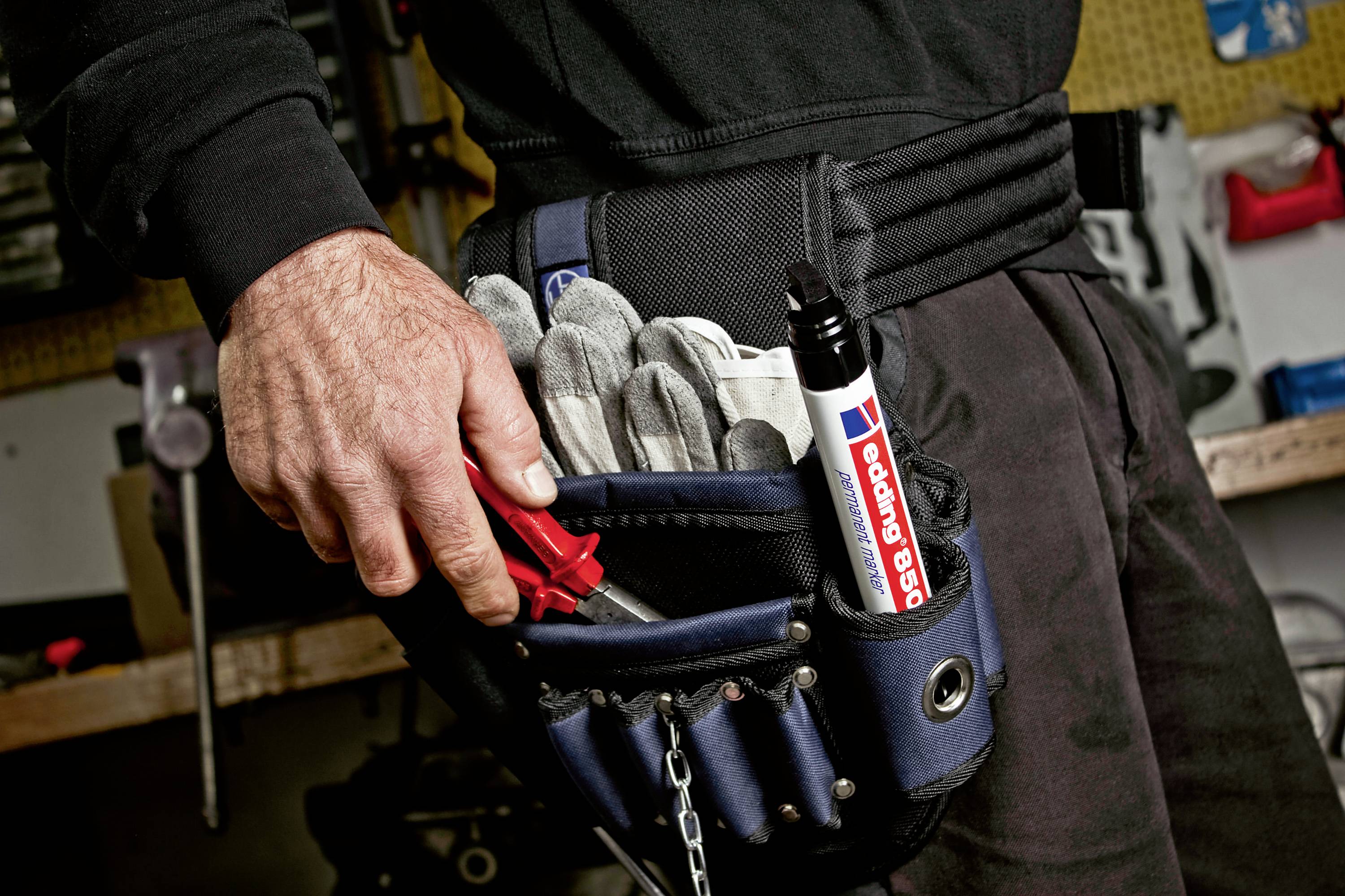 Ein Handwerker hält eine rote Zange in der Hand. In einem schwarzen Werkzeuggürtel stecken Arbeitshandschuhe und ein großer Marker.