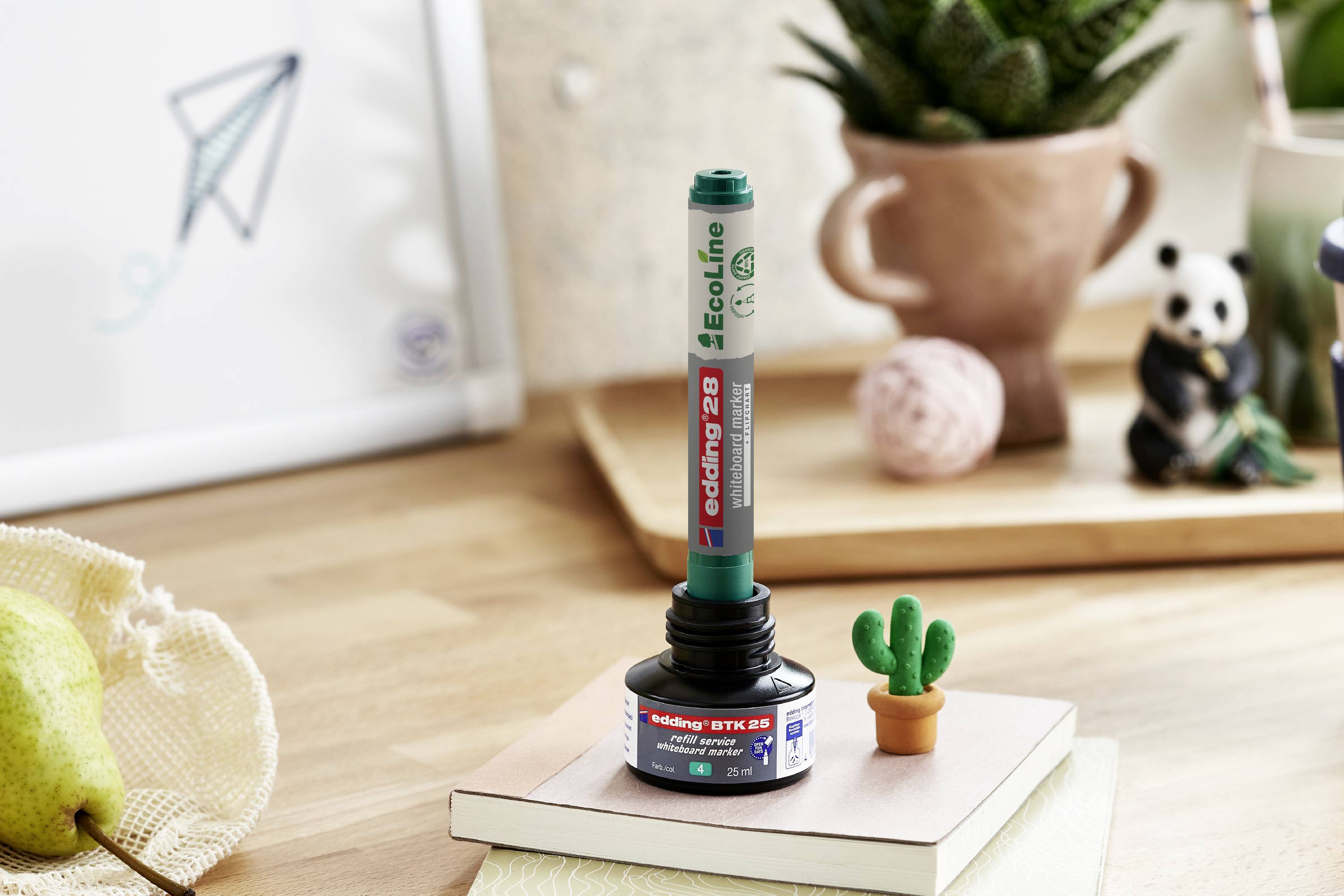Nachfüllbarer Filzstift 'edding EcoLine 28' in Tintenflasche, mit kleinem Kaktus und Dekorationen, auf Holztisch arrangiert.