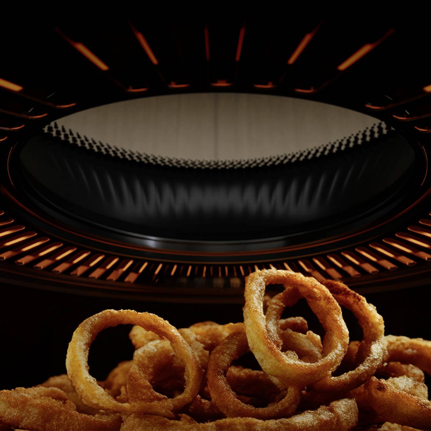 Zwiebelringe auf einem Küchengerät, das sie von oben erhitzt. Die Ringe sind knusprig gebraten und braun.