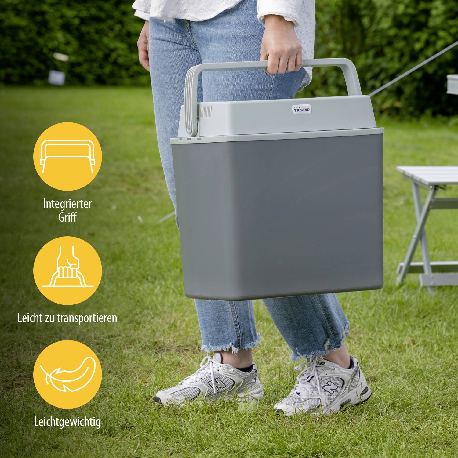 Person steht auf Gras und hält eine tragbare, graue Kühlbox mit integriertem Griff. Drei Symbole zeigen Benutzerfreundlichkeit: integrierter Griff, leicht zu transportieren, leichtgewichtig.