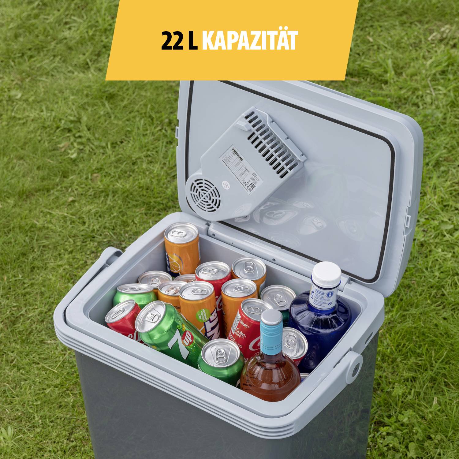 Geöffnete Kühlbox mit 22 Litern Kapazität, gefüllt mit diversen Getränkedosen und Flaschen, stehend auf einer Rasenfläche.