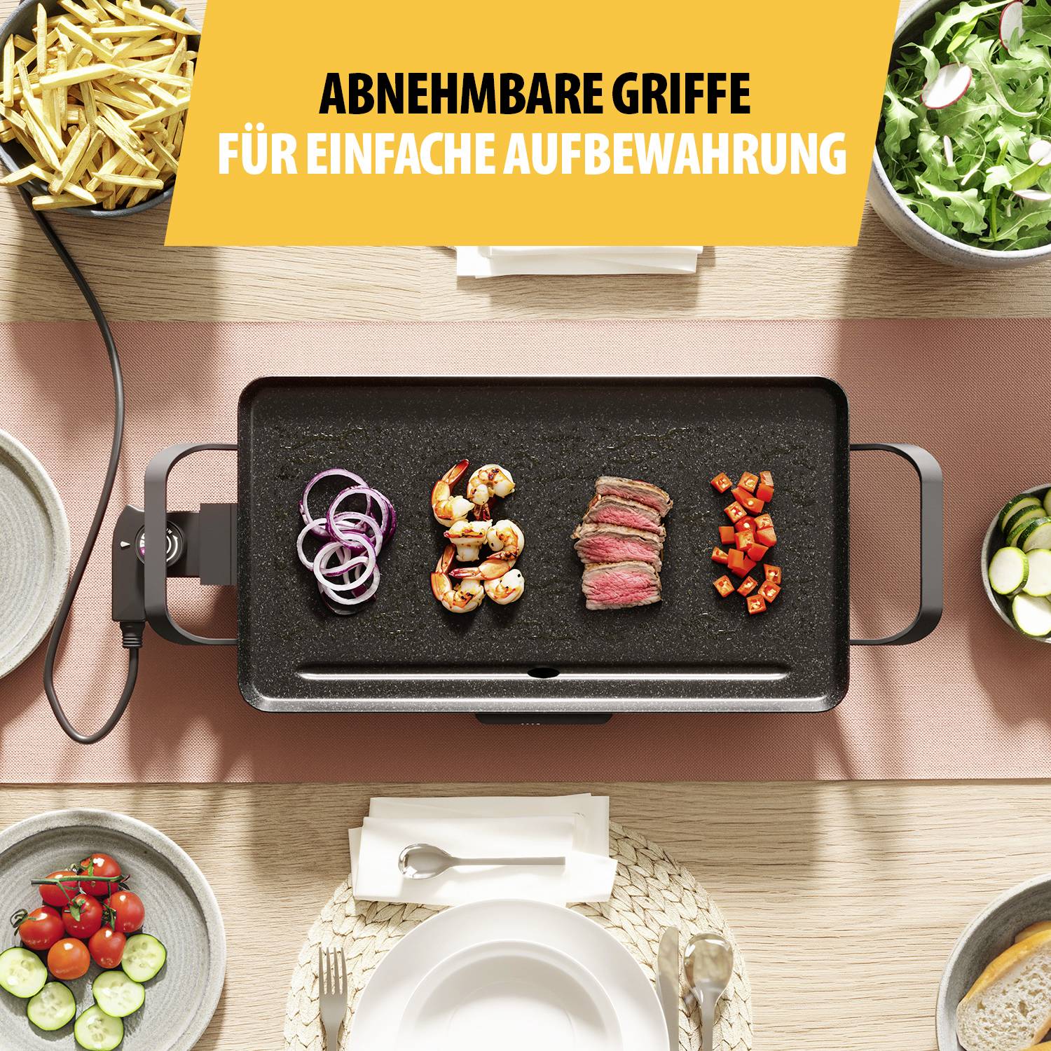 Eine elektrische Grillplatte mit Garnelen, rotem Fleisch und Gemüse. Oben links sind Pommes und Salat zu sehen, mit Besteck und Teller.