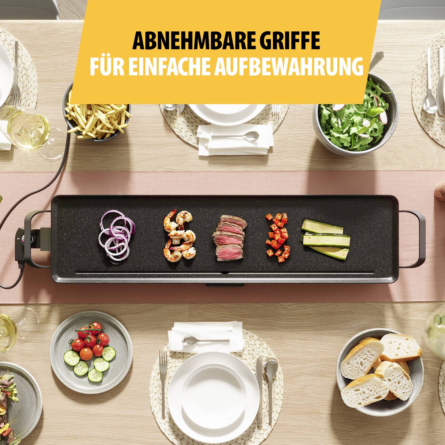 Schwarzer Grill mit Gemüse und Fleisch auf Tisch, gelbes Banner mit Text 'ABNEHMBARE GRIFFE FÜR EINFACHE AUFBEWAHRUNG'. Teller und Salate im Hintergrund.