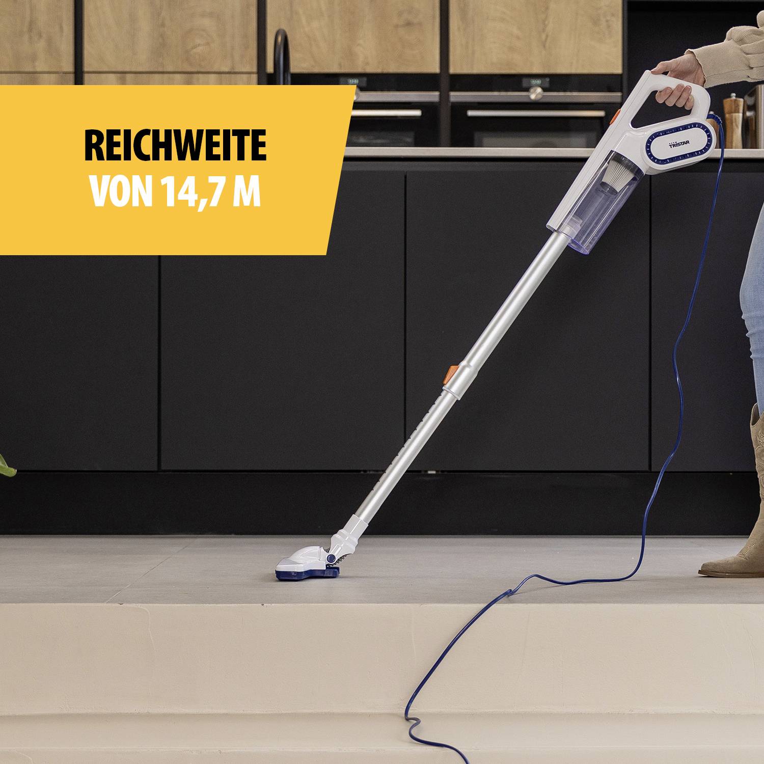 Ein Staubsauger wird von einer Person auf hellem Boden benutzt. Text auf dem Bild: 'Reichweite von 14,7 m'.